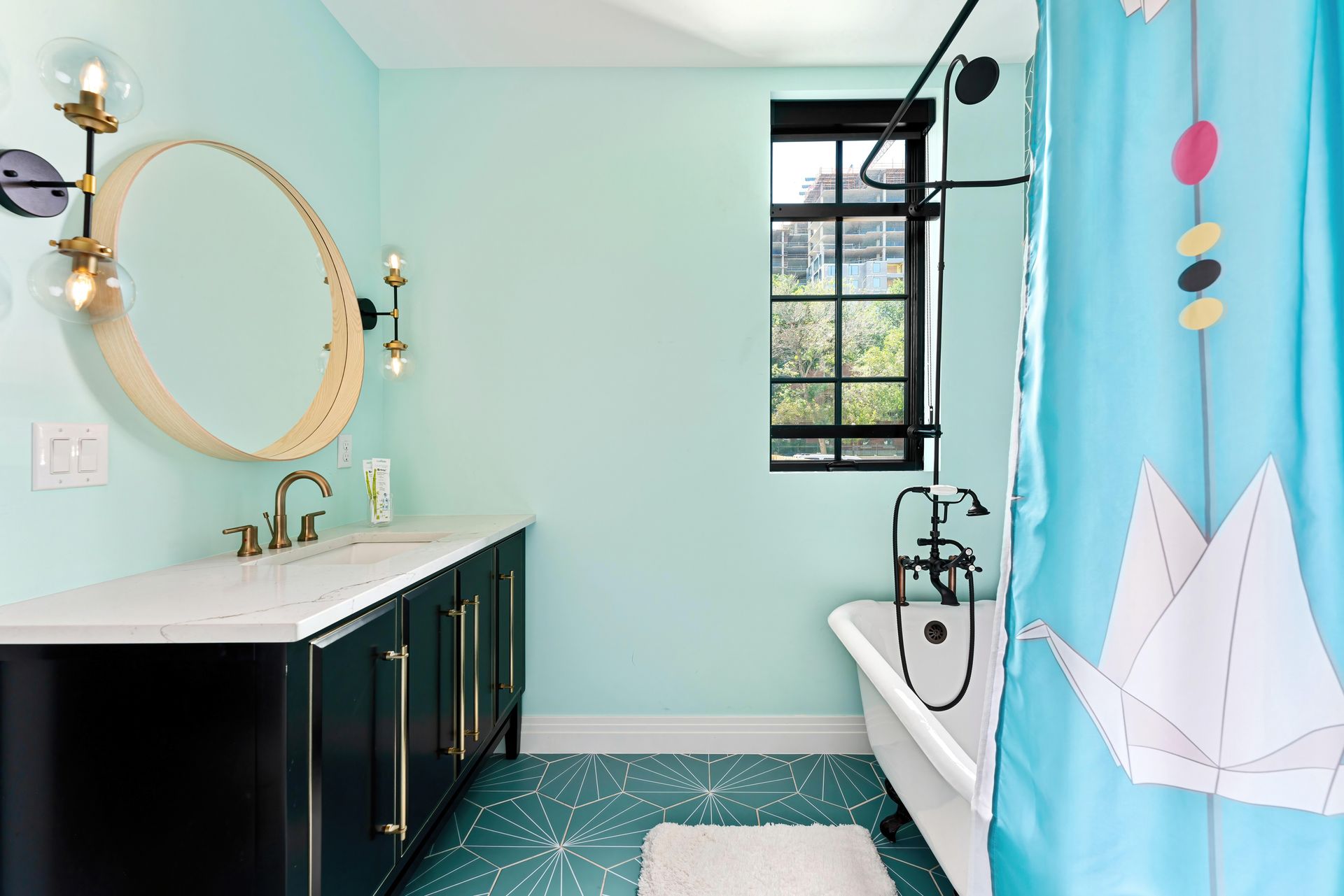 Mint-green bathroom with dark vanity, round mirror, window, and blue shower curtain with paper-boat print