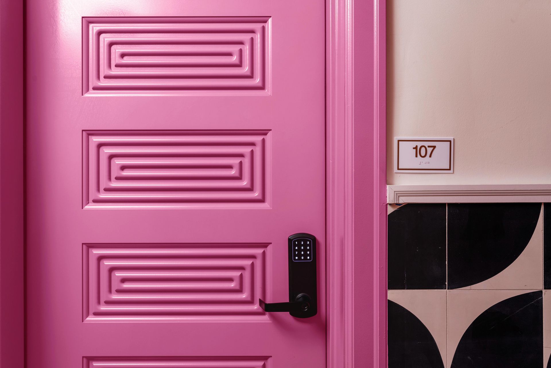 Pink paneled door with keypad lock beside a wall-mounted room number 107 sign