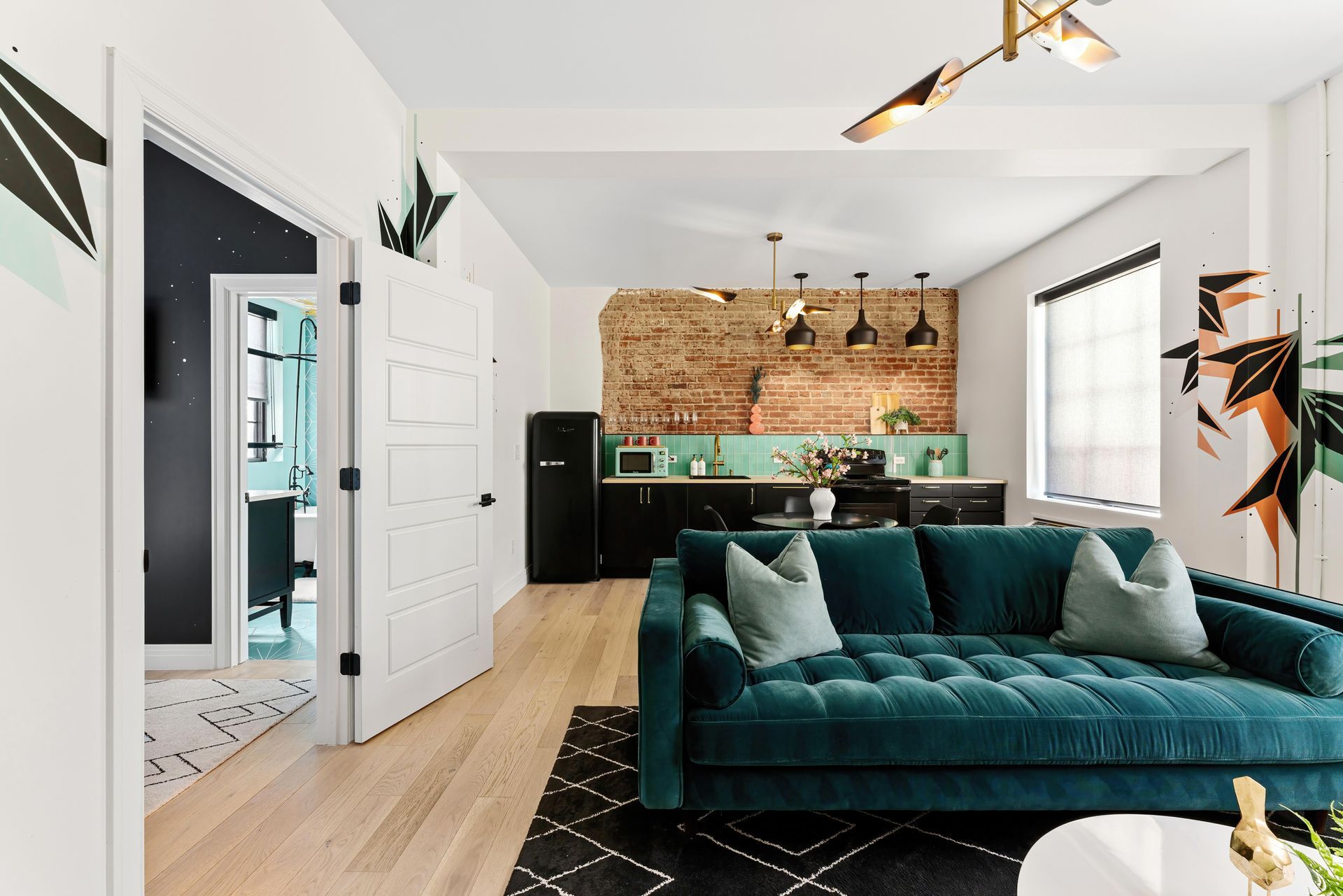 Modern living room with teal sofa, black rug, wood floors, and a kitchen in the background