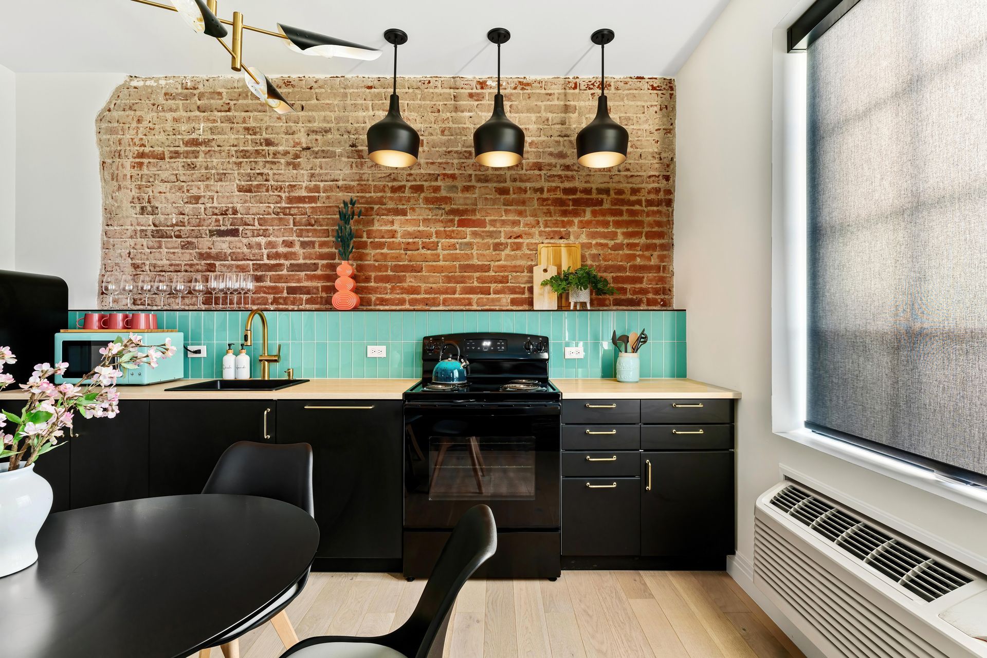 Modern kitchen with black cabinets, turquoise backsplash, brick wall, and hanging pendant lights