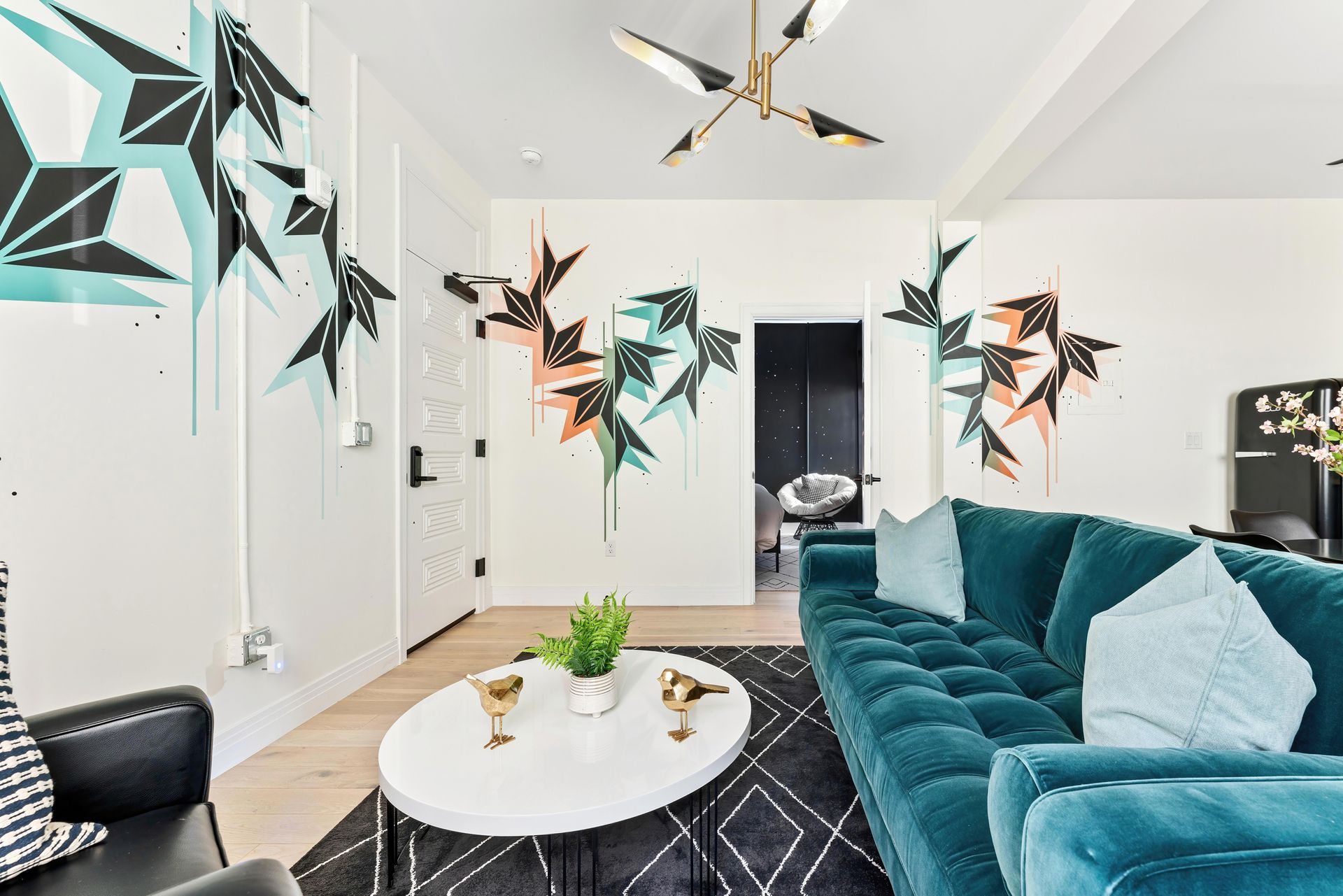 Modern living room with teal sofa, white coffee table, black rug, and geometric wall art
