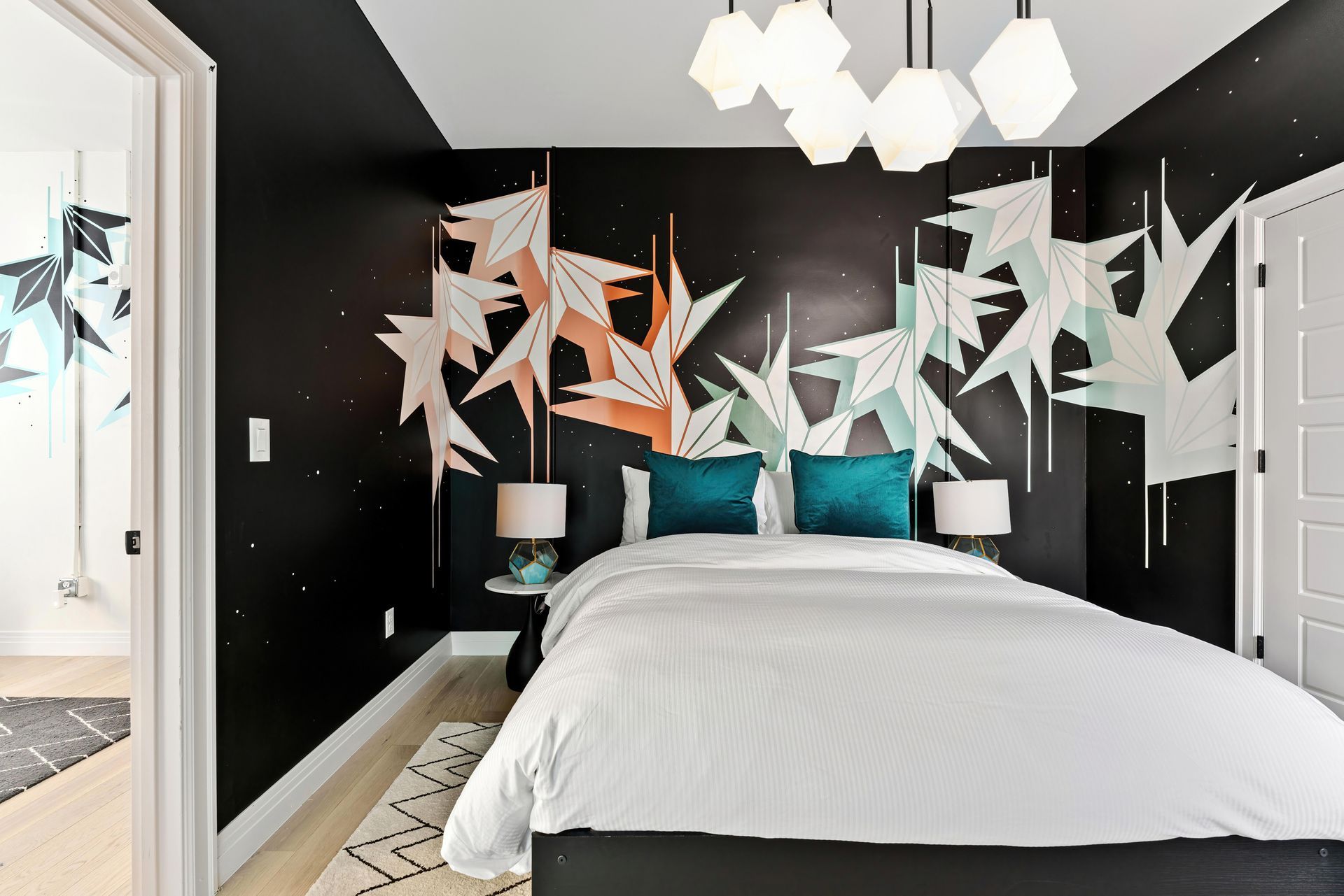 Modern bedroom with black walls, white bed, teal pillows, and geometric wall art above the headboard
