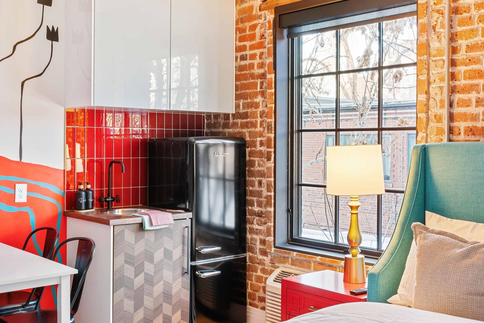 Bright living room corner with red wall, black refrigerator, window, lamp, and armchair