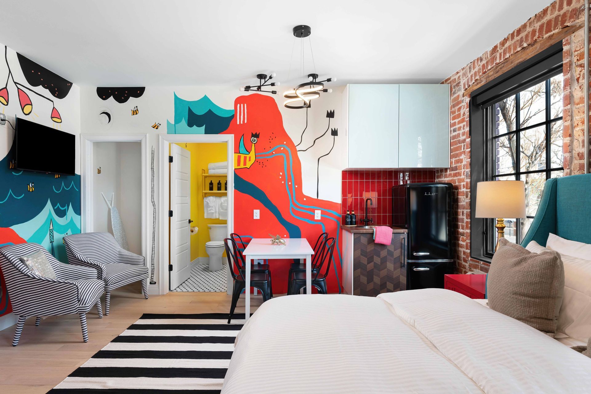 Colorful bedroom with bold red mural, zebra chair, striped rug, white bed, and black-framed windows