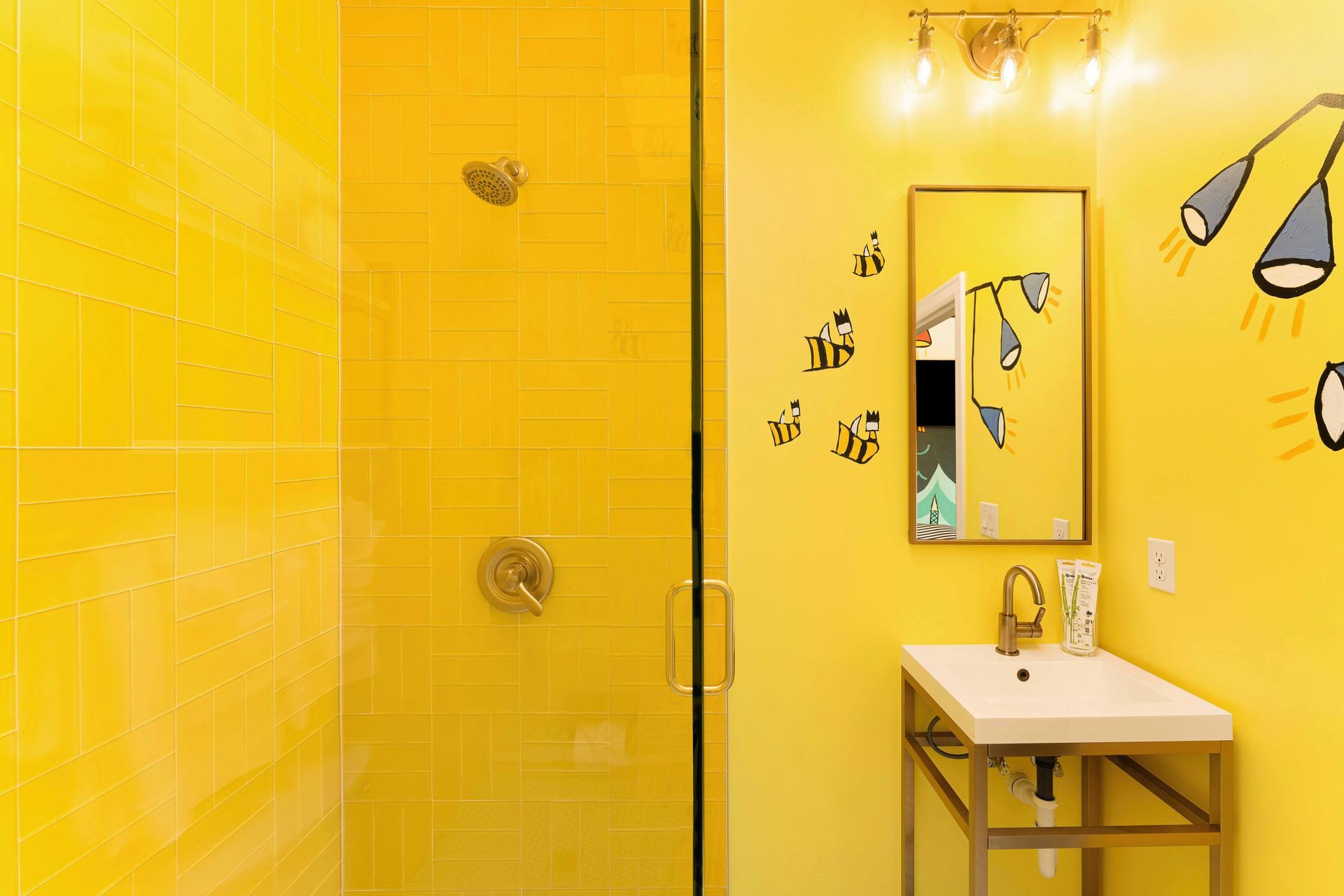 Bright yellow bathroom with a glass shower, mirror, and sink vanity featuring playful black wall drawings.