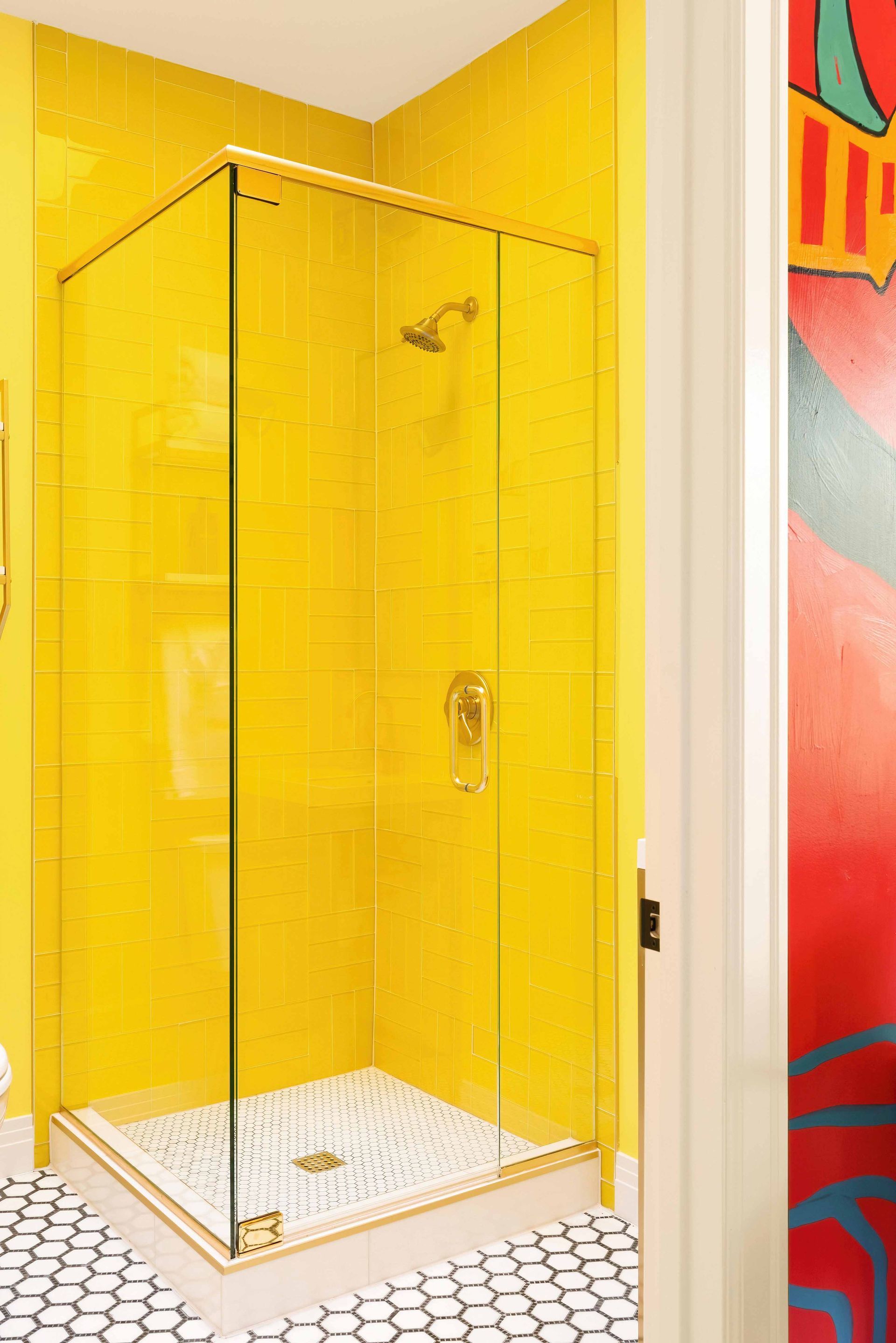 Yellow-tiled shower stall with glass door and white pebble floor in a bright bathroom