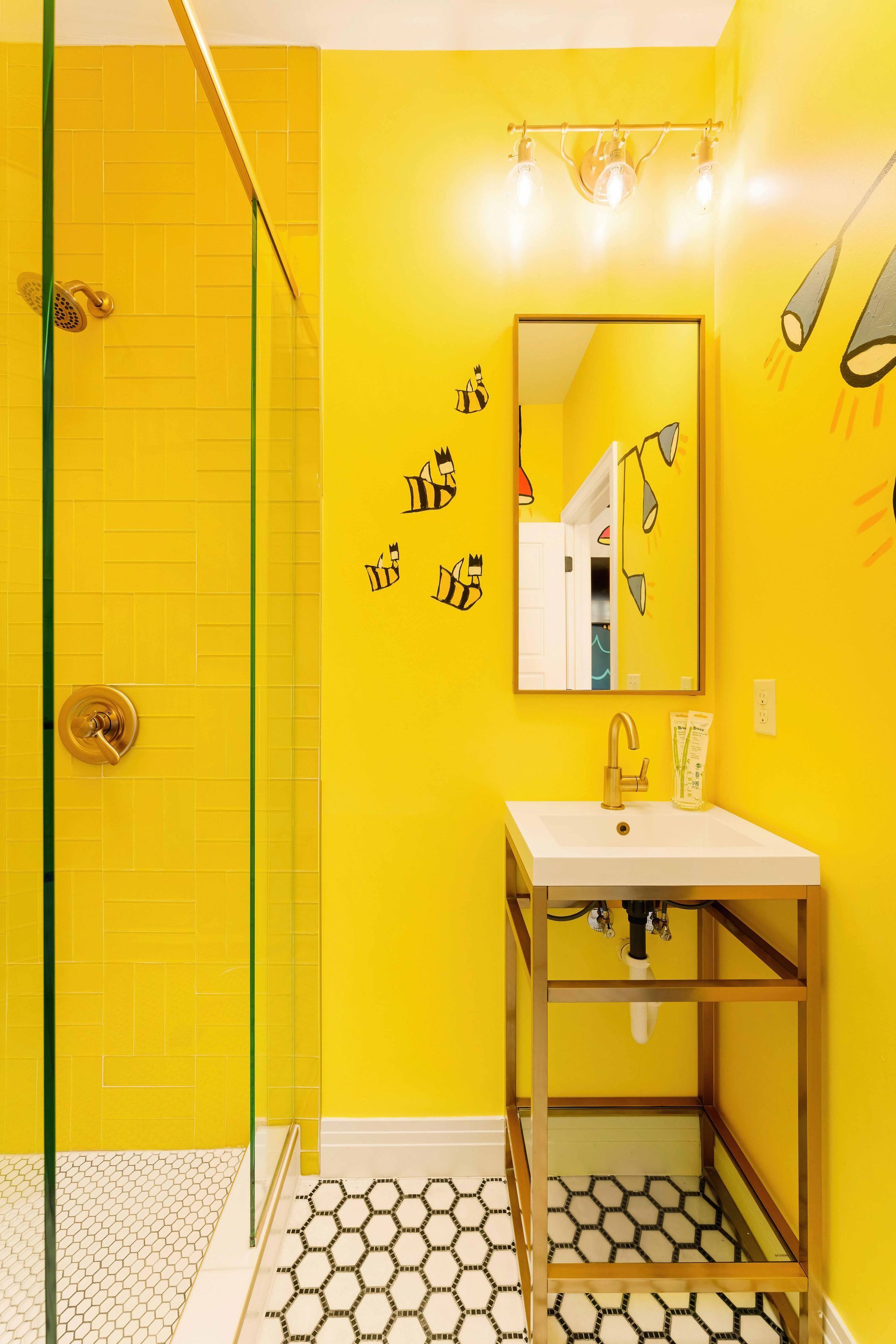 Bright yellow bathroom with glass shower, white sink, mirror, and hexagonal tile floor
