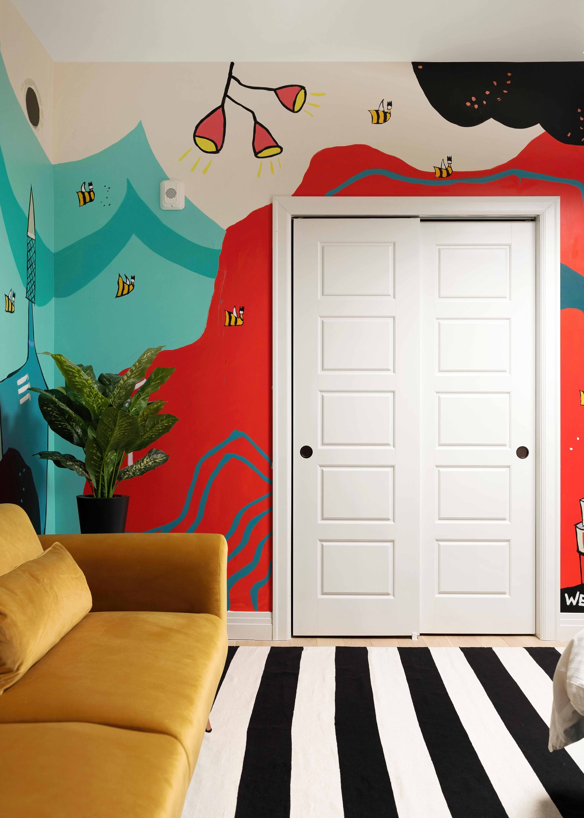 Colorful mural wall with white double doors, black-and-white striped floor, and a mustard sofa.
