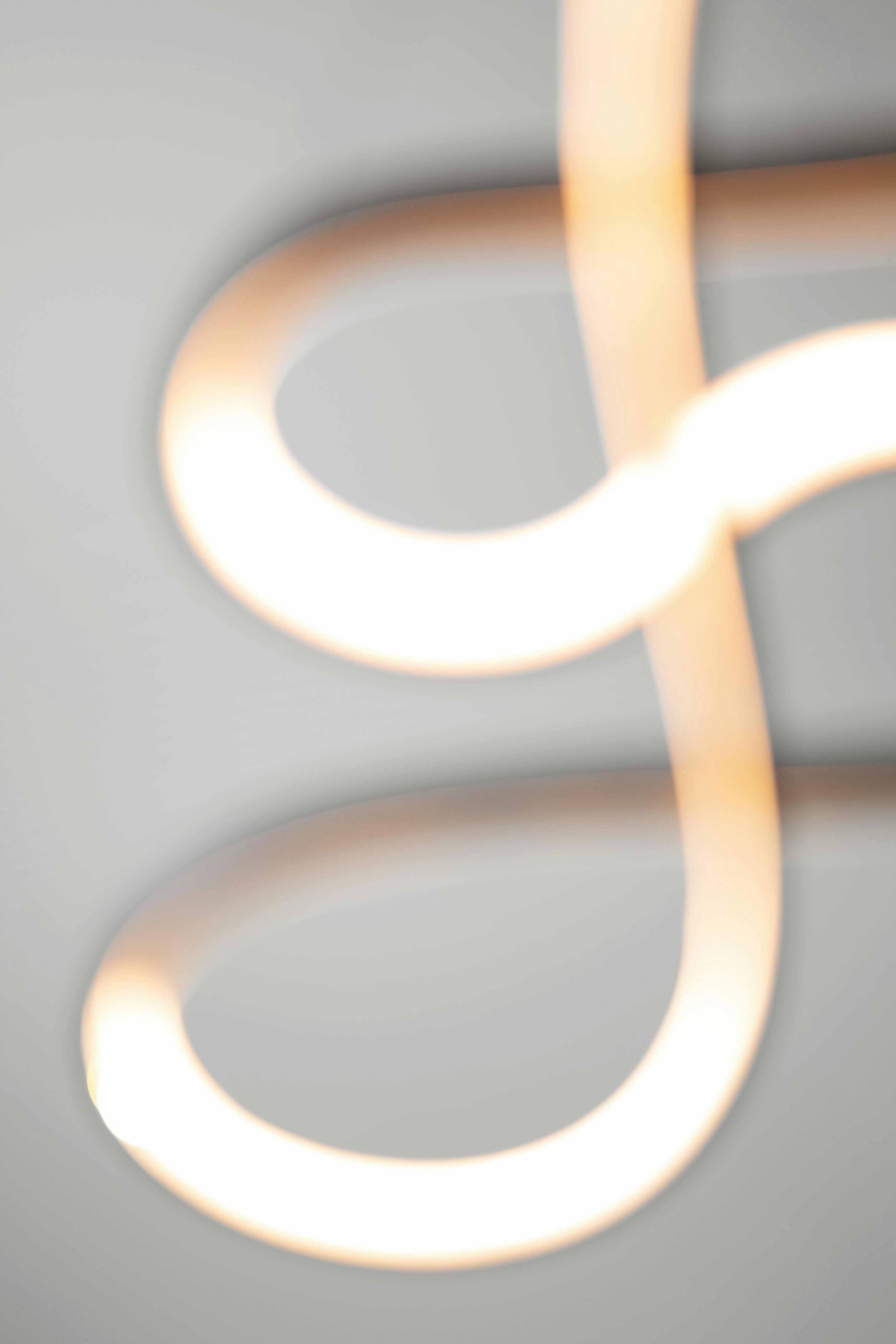Close-up of a glowing white looped light fixture against a gray wall.