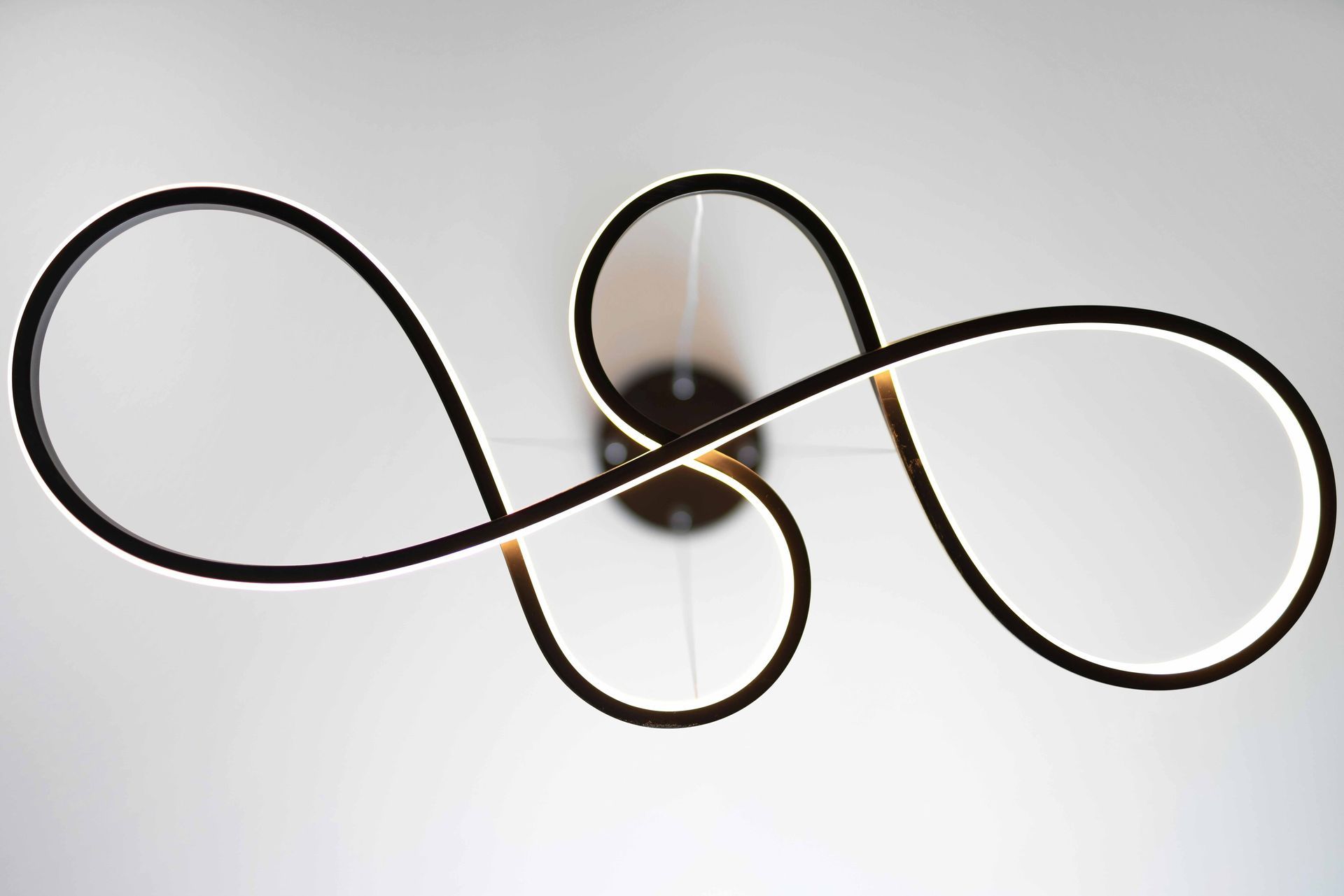Abstract black looped cord on a white background, forming an infinity-like shape around a central light fixture.