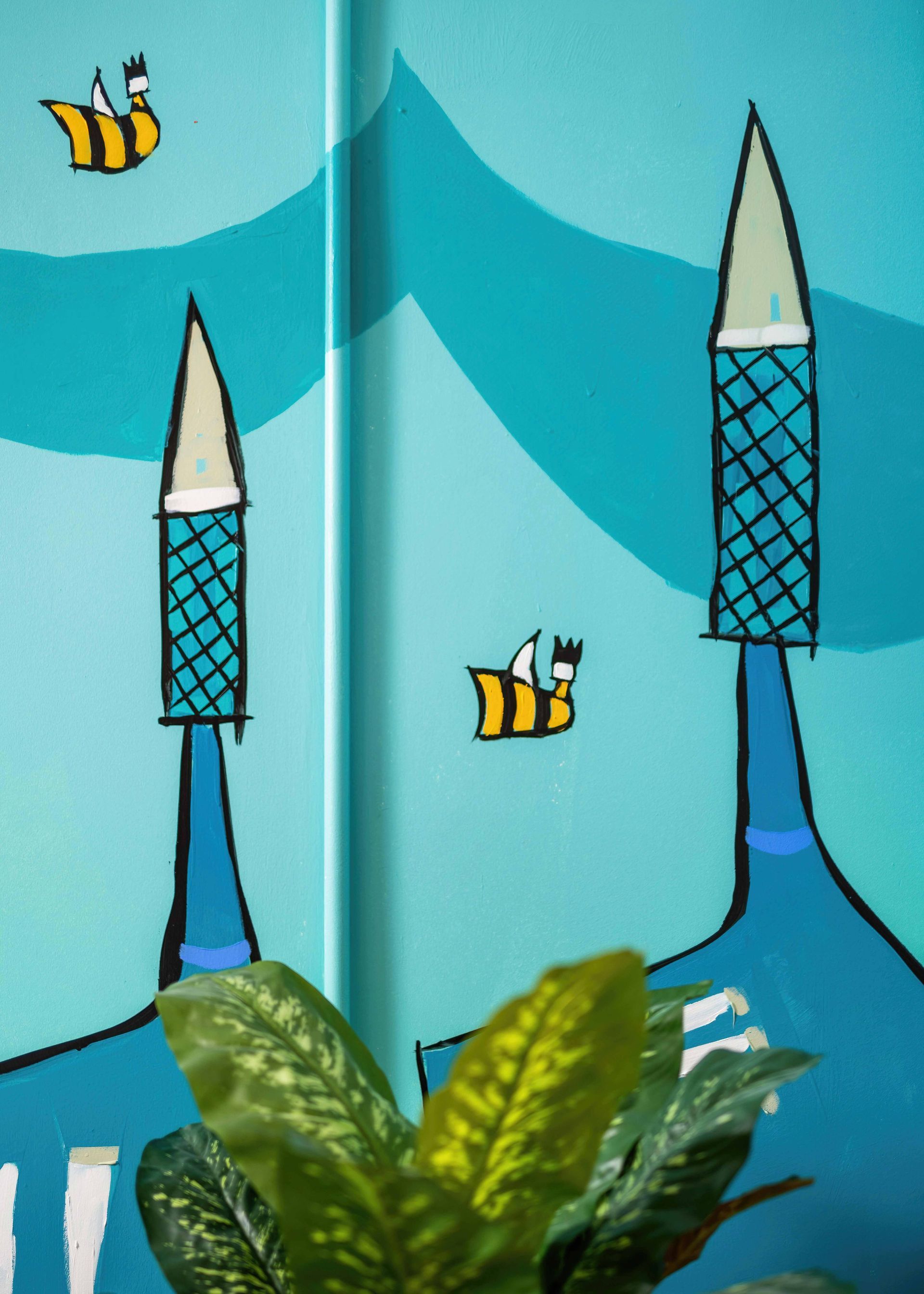 Blue drawing of two tall towers with yellow birds flying over green leaves