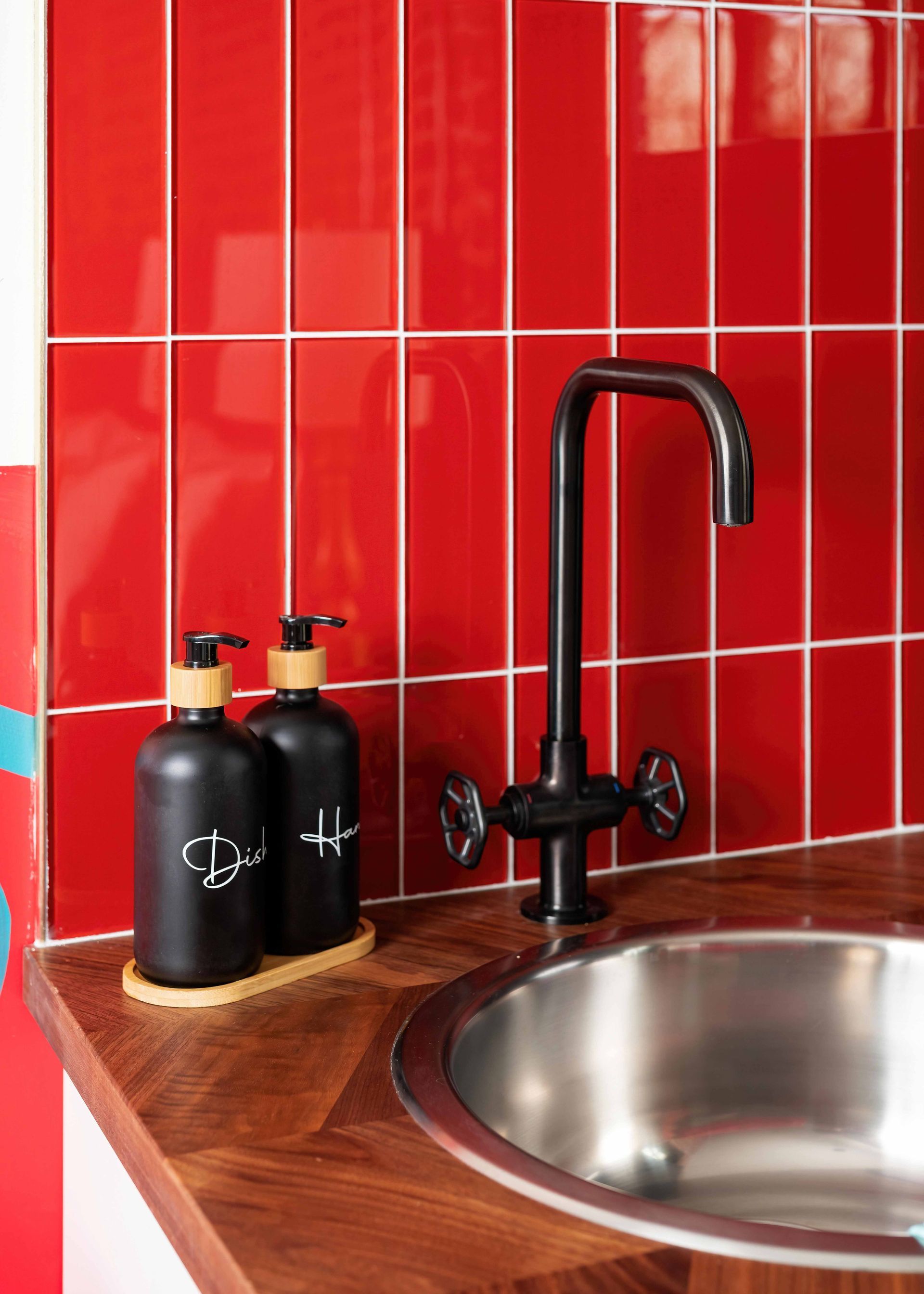Red-tiled kitchen corner with black faucet, round sink, wooden counter, and two black bottles