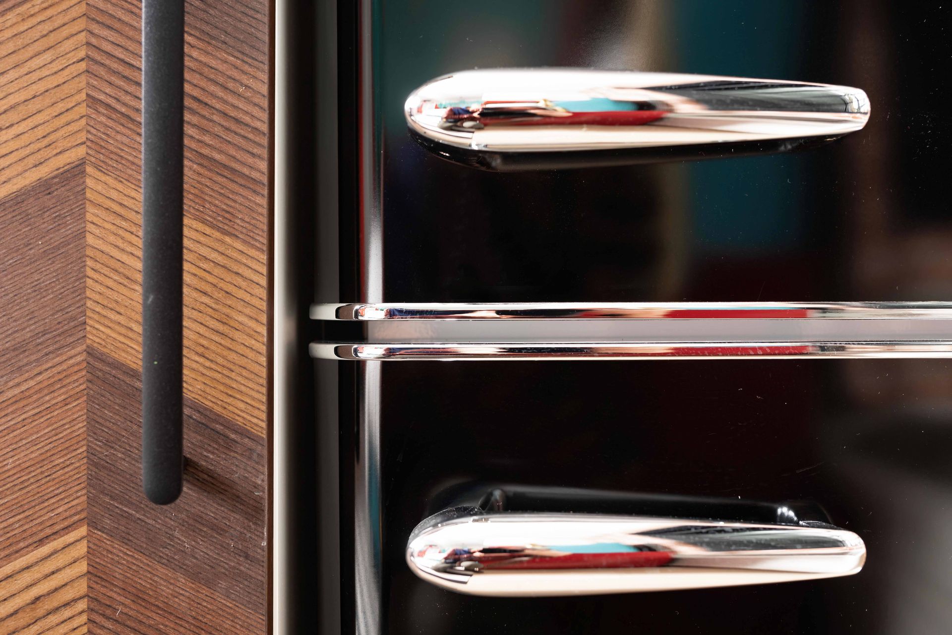 Close-up of chrome drawer handles on a dark cabinet beside a wood-grain panel