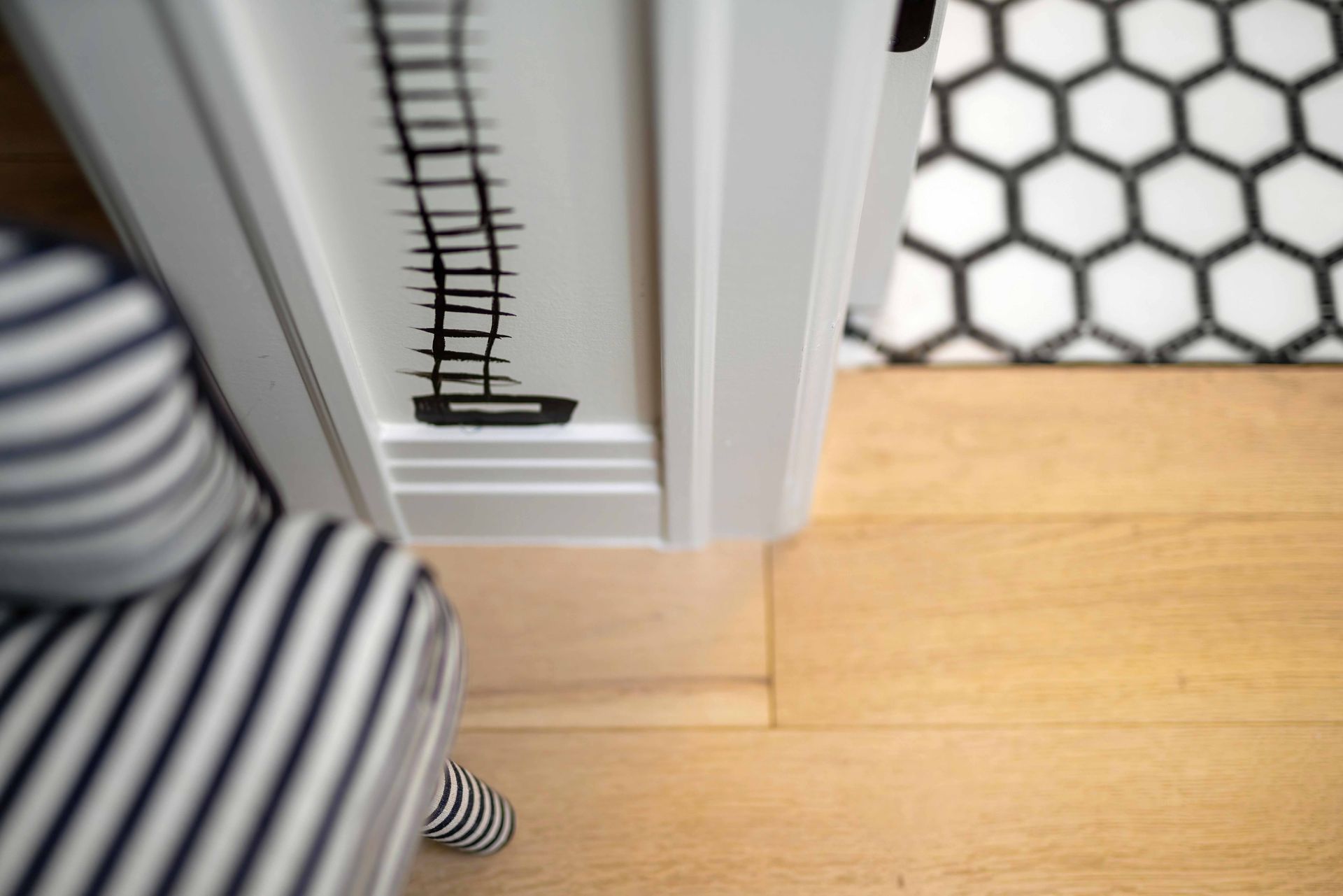 Striped clothing beside a white doorframe and wood floor, with a honeycomb-patterned wall or gate nearby