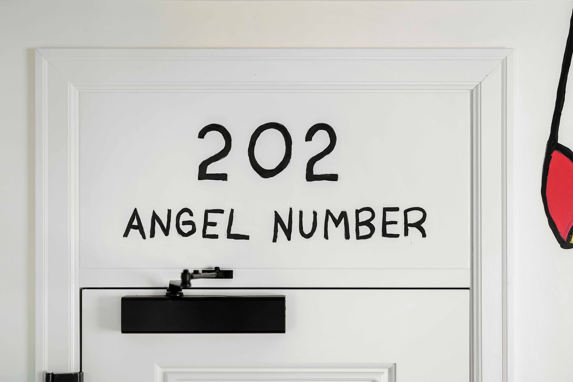 White door labeled “202” and “ANGEL NUMBER” with a black door closer at the top