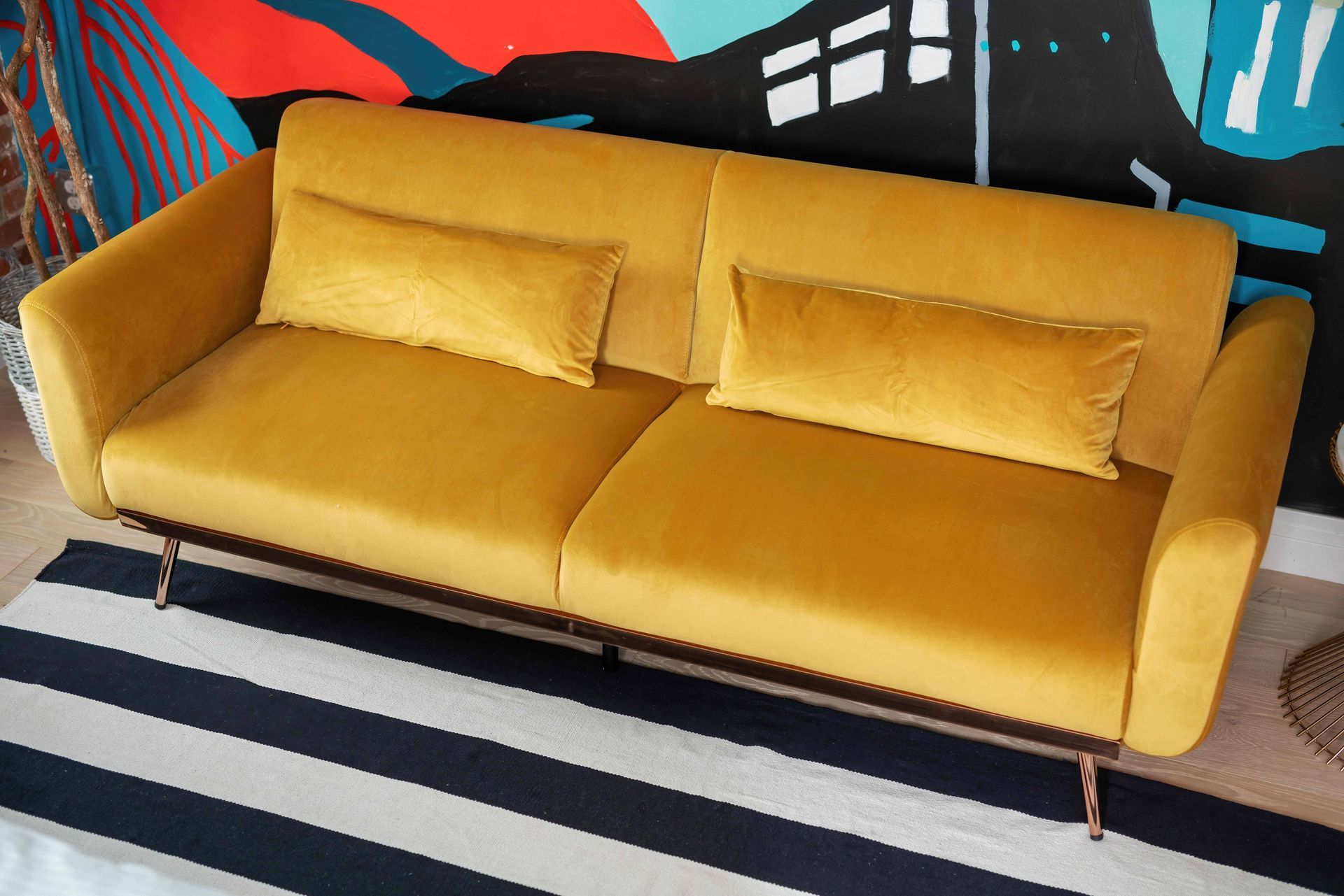 Mustard yellow sofa with matching pillows on a striped rug in a colorful room