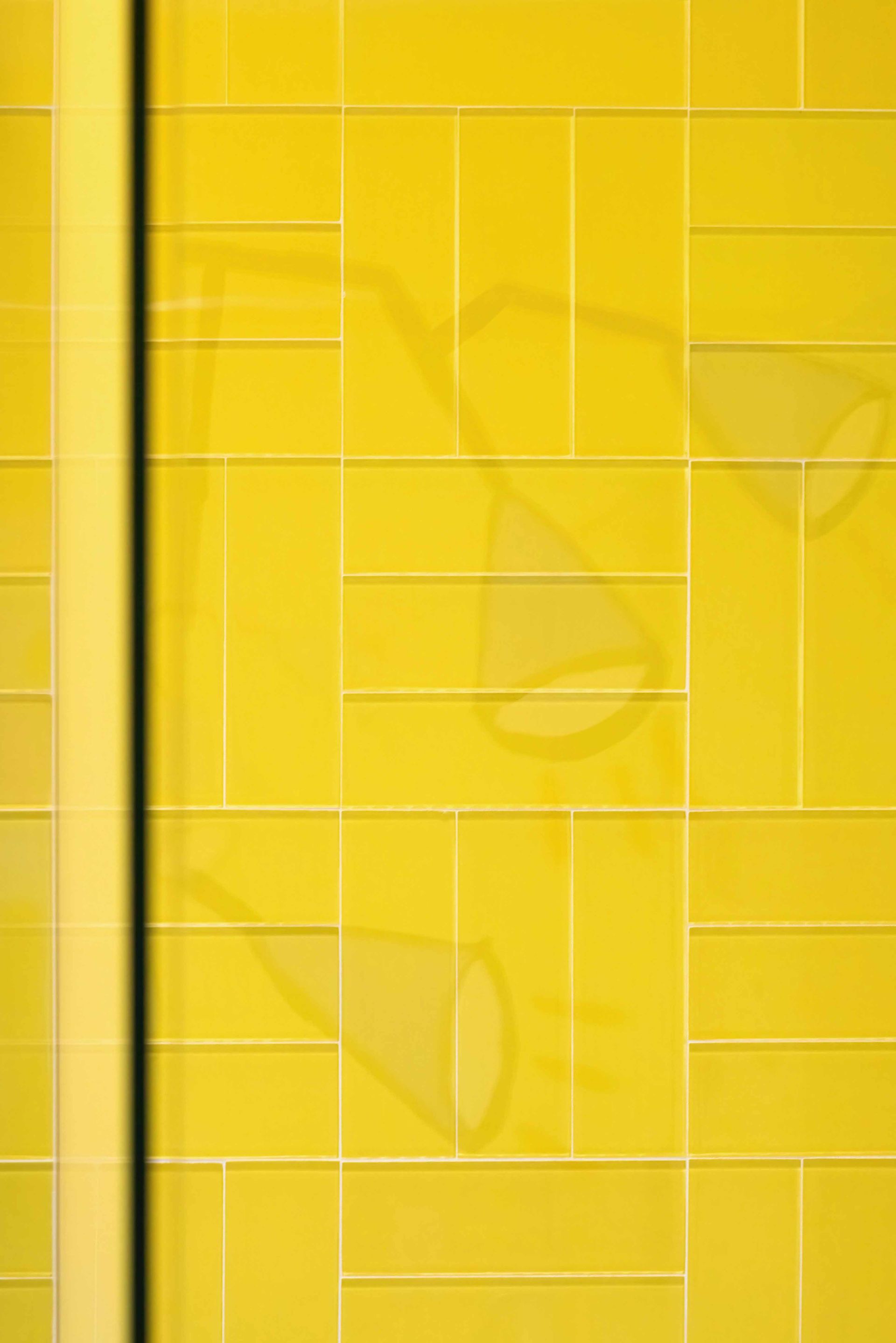 Yellow tiled wall with faint geometric patterns and reflections