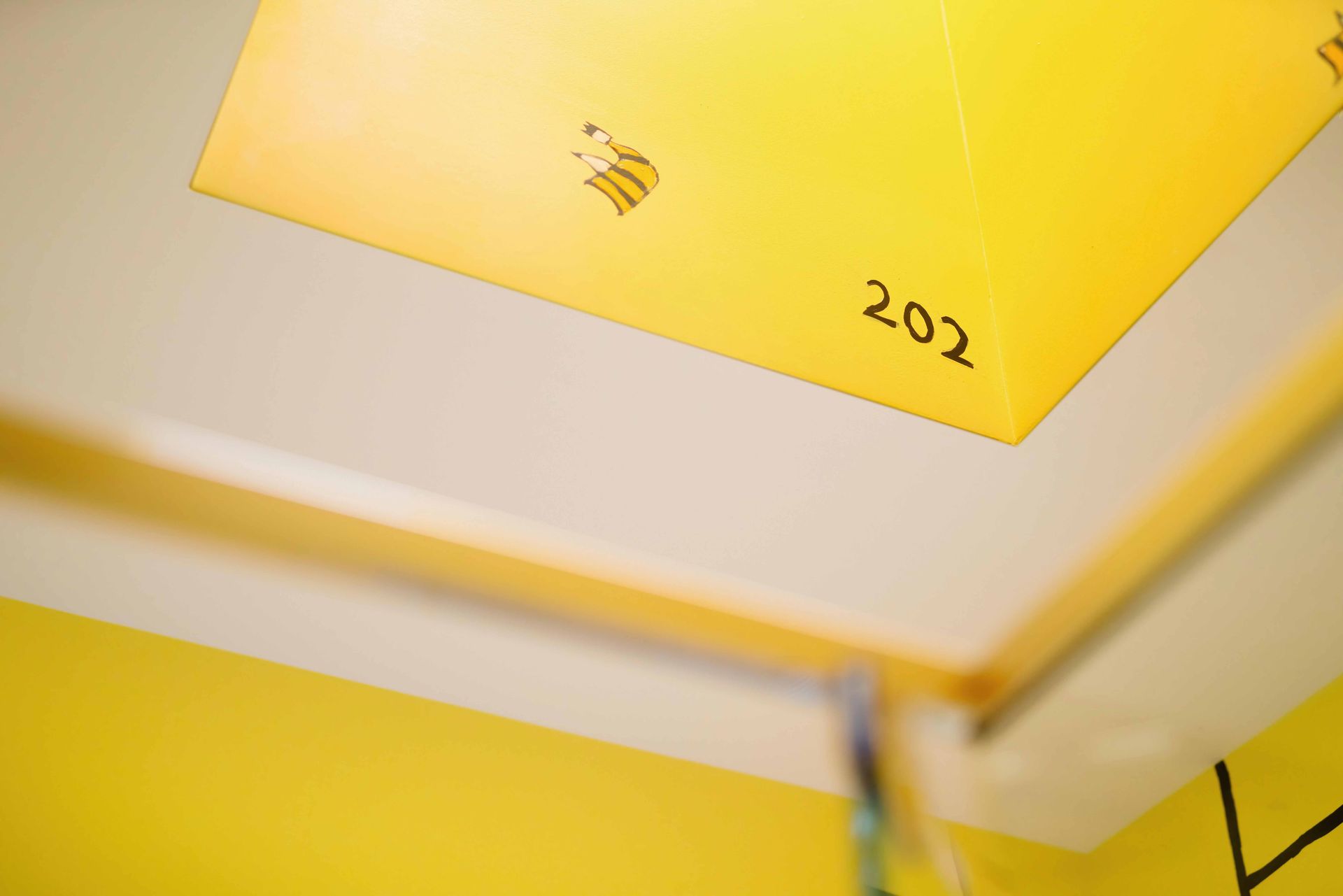 Yellow ceiling sign with the number 202 in a bright indoor hallway