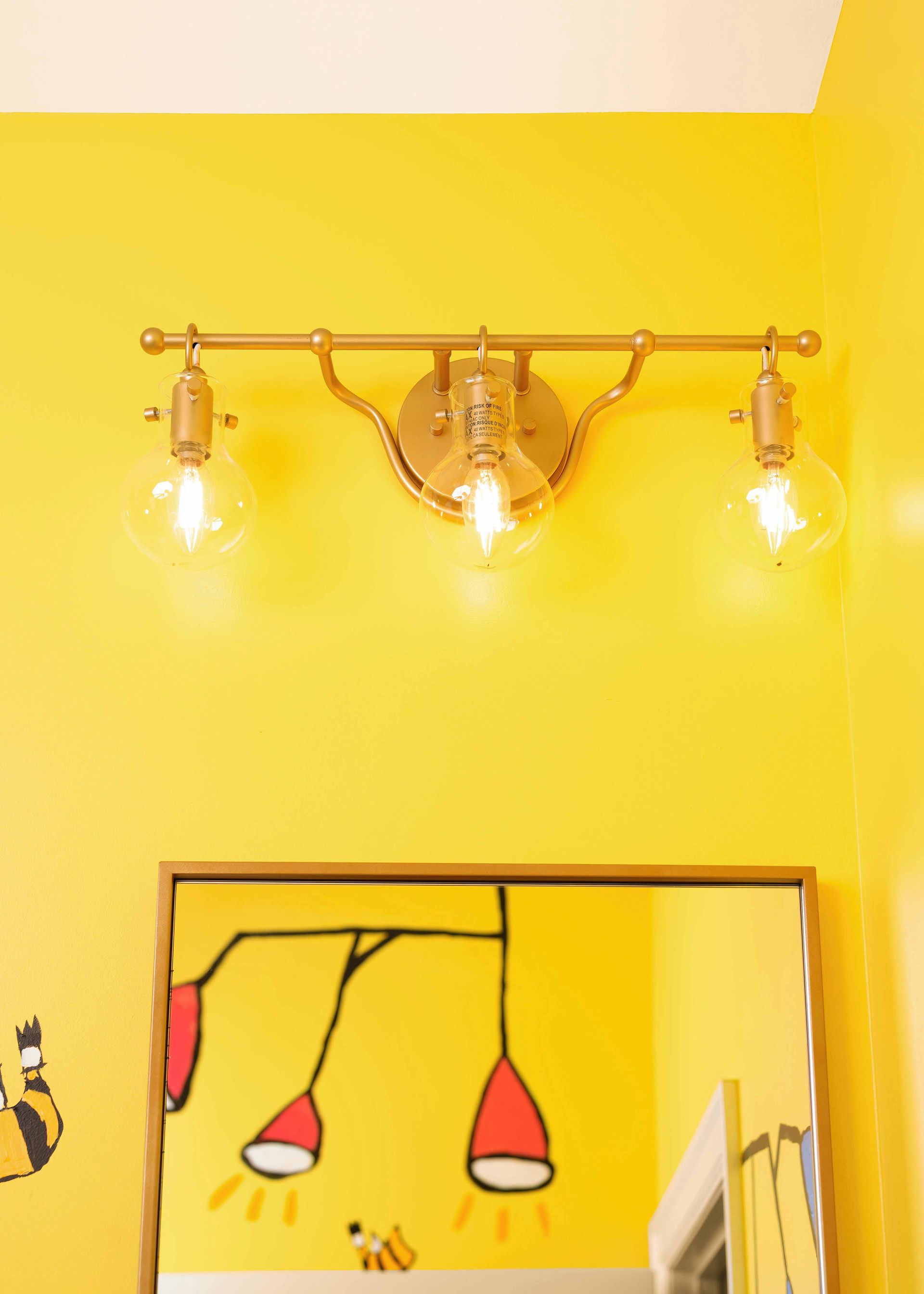 Yellow wall with three glowing wall sconces above a framed abstract drawing