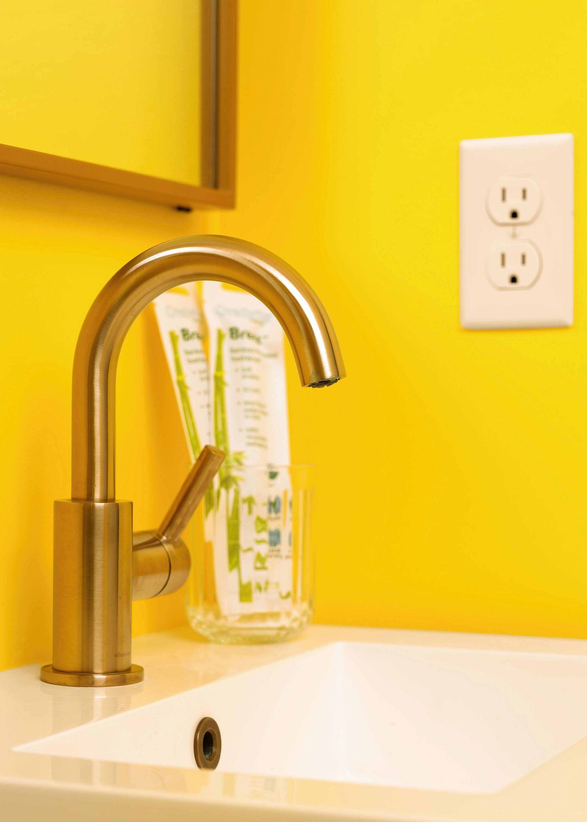 Yellow bathroom sink with brass faucet and wall outlet on a bright yellow wall