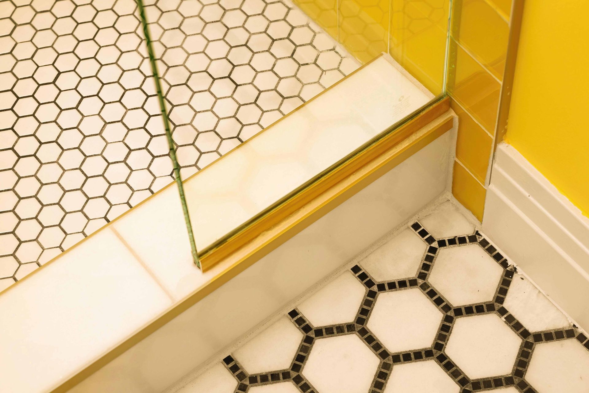Bathroom corner with yellow walls, glass shower door, and black-and-white hex tile floor
