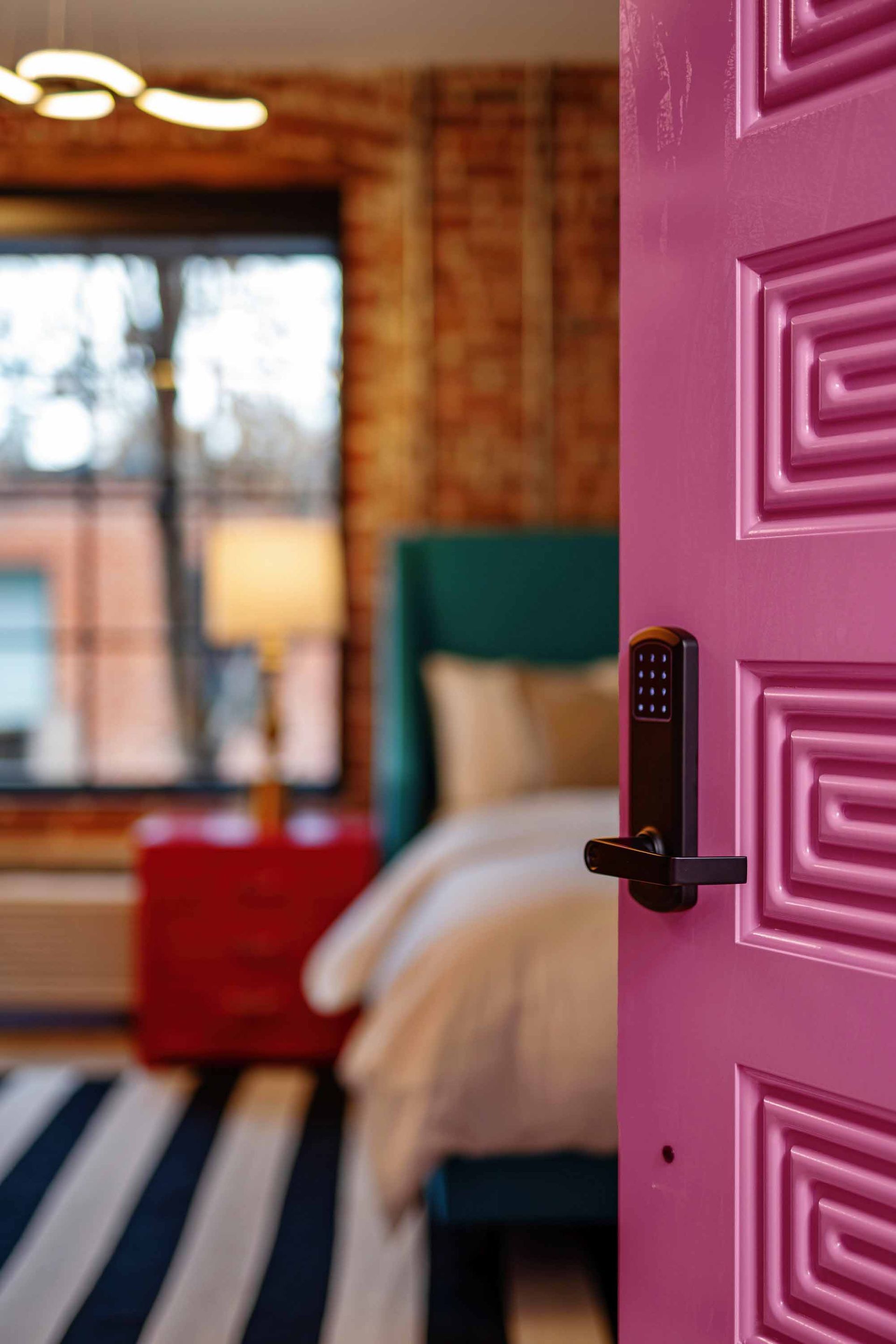 Open pink door to a cozy bedroom with a teal headboard and striped rug