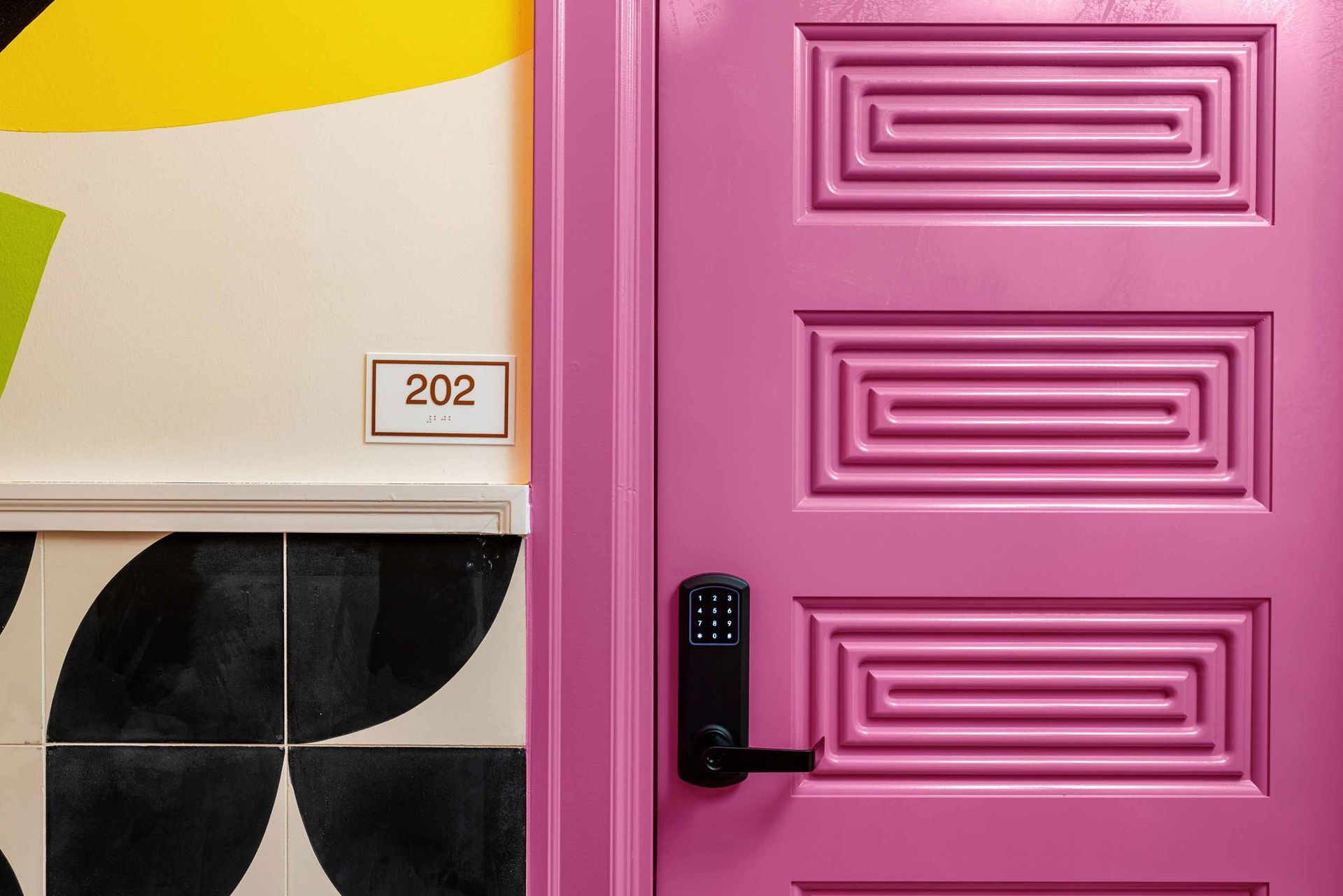 Pink front door with black handle beside a small numbered wall panel reading 202
