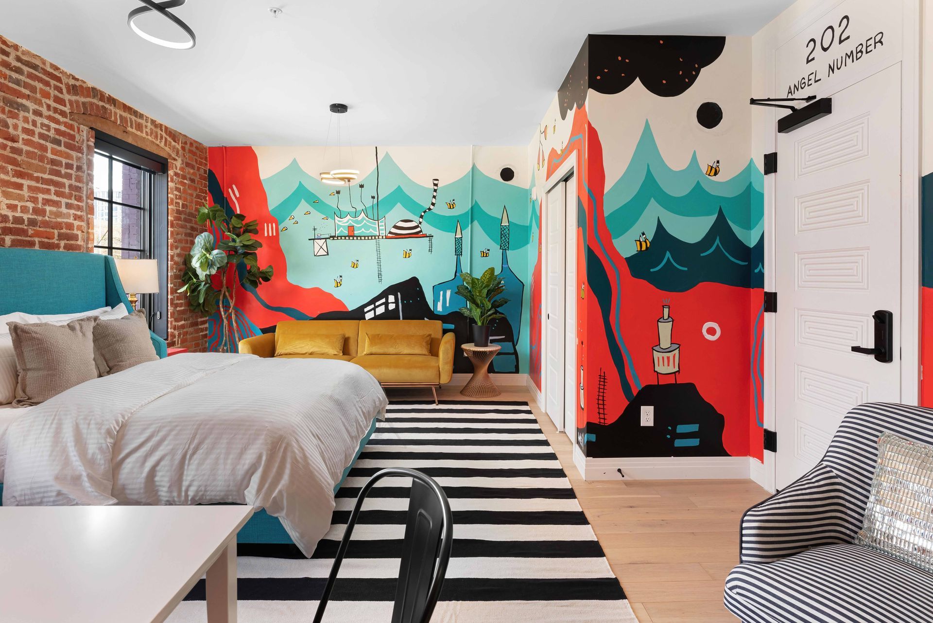 Colorful modern bedroom with mural walls, striped rug, white bed, and chair by a window