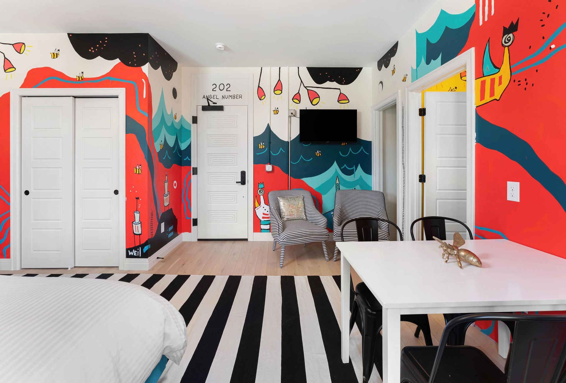 Colorful bedroom with bold abstract wall art, white doors, zebra chairs, and black-and-white striped rug