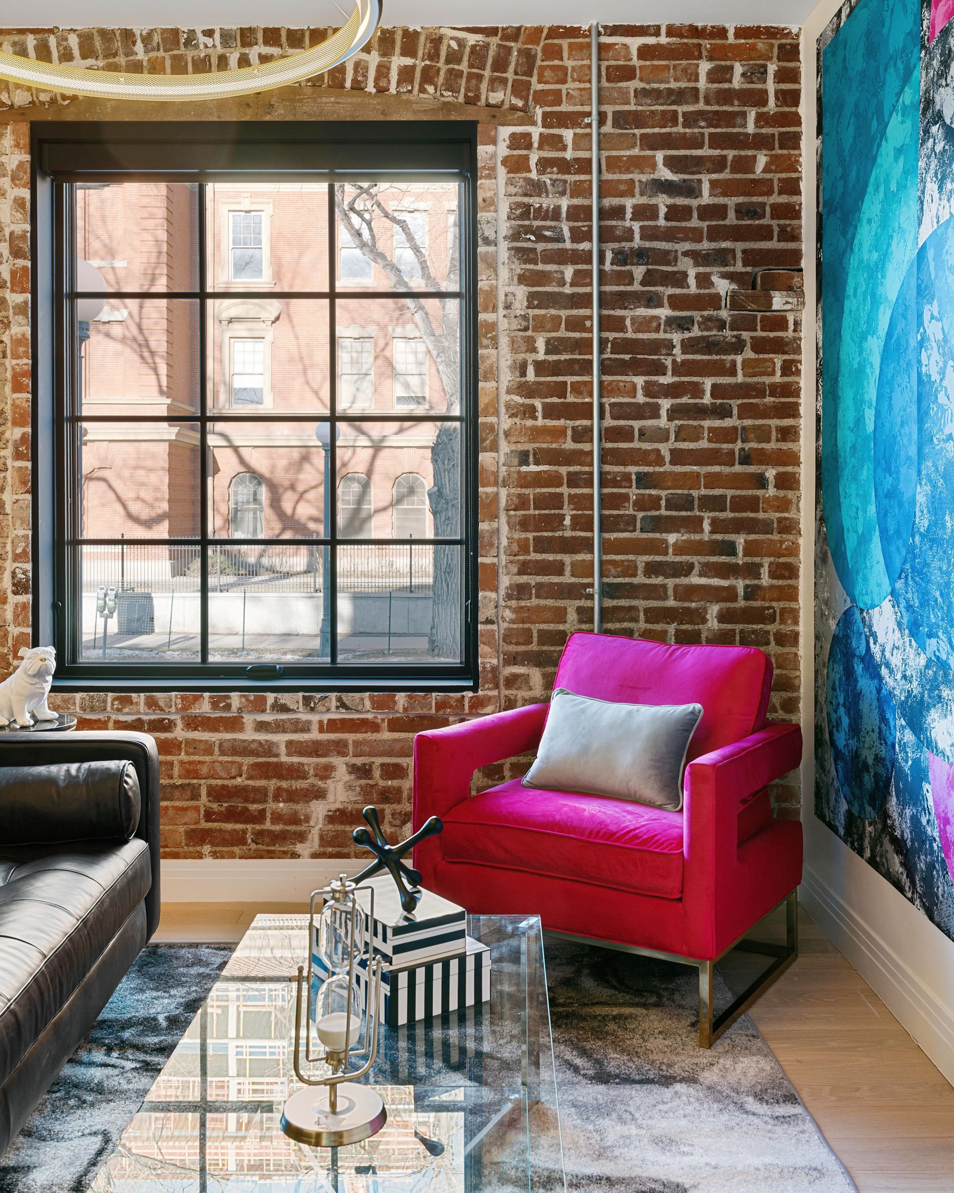 Loft living room with exposed brick, large window, bright pink chair, and blue accent wall.