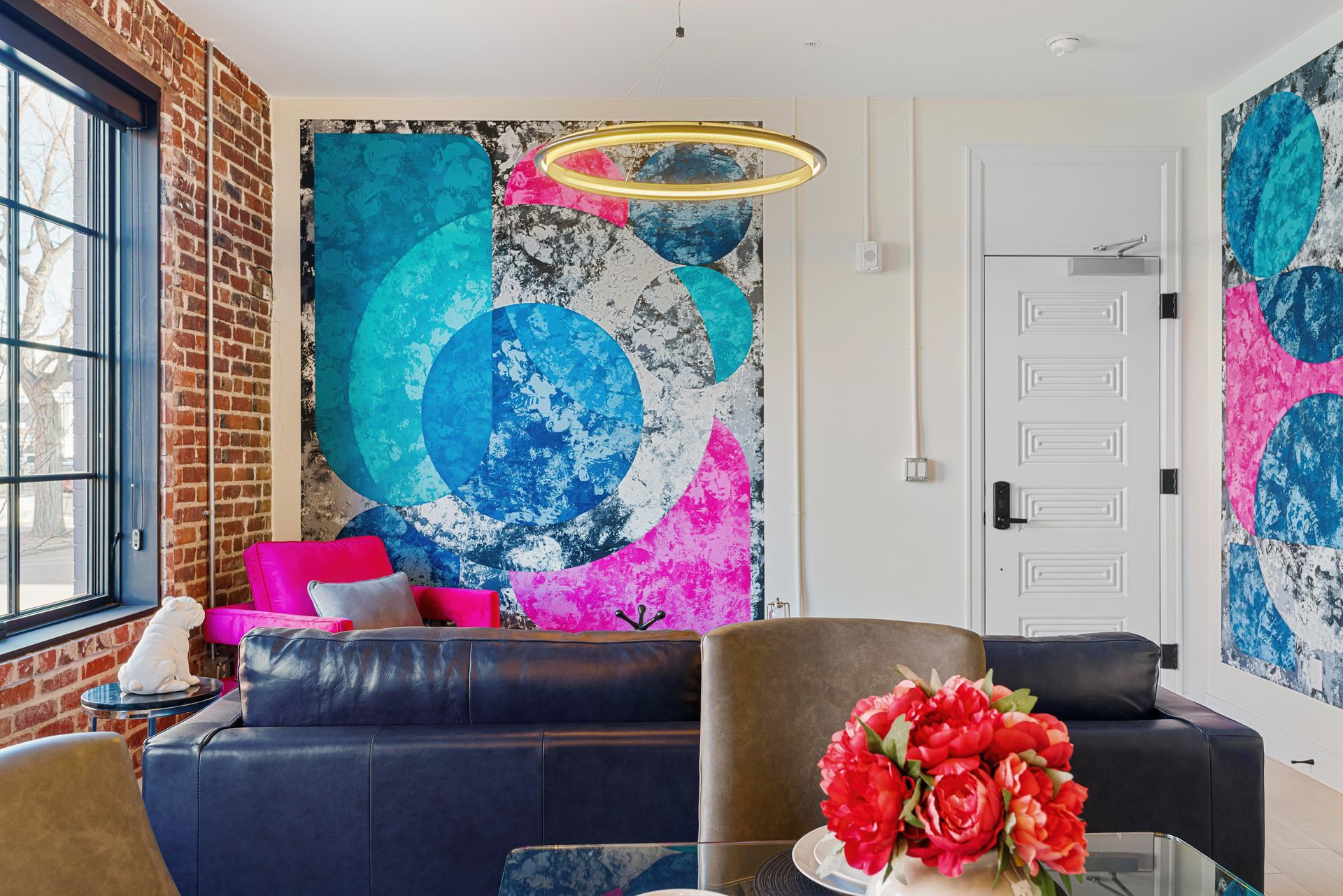 Bright modern living room with bold abstract wall art, black sofa, brick window wall, and pink accents
