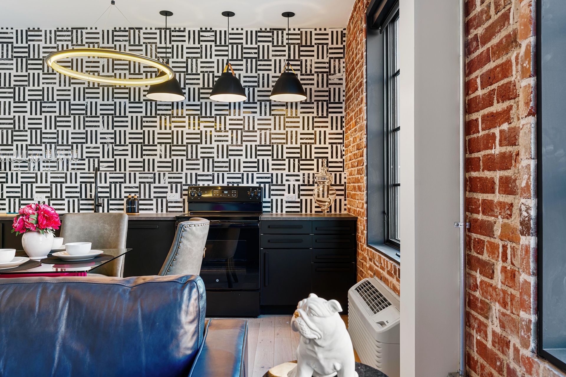 Modern dining area with black-and-white patterned wallpaper, brick wall, pendant lights, and a table with flowers.