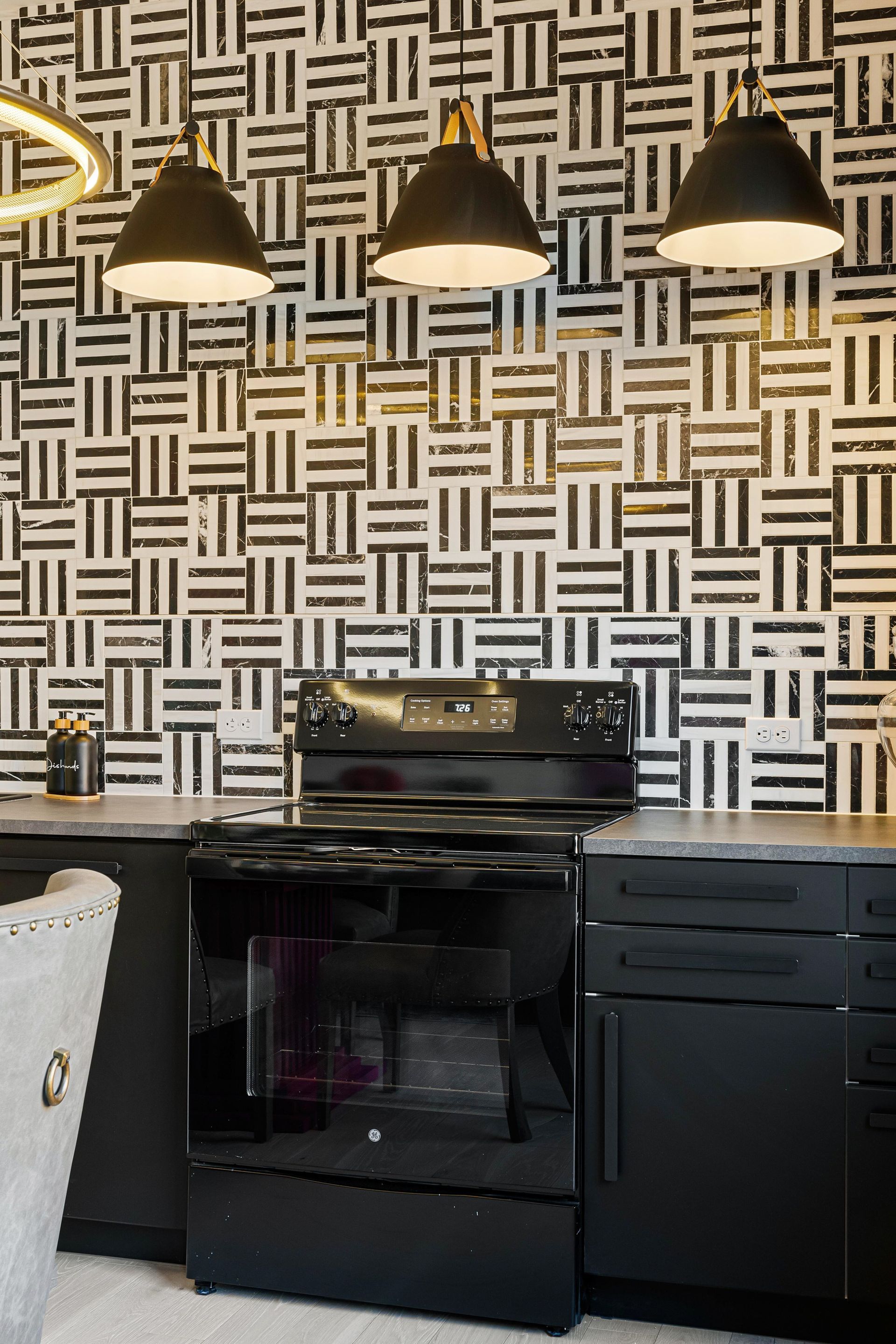 Modern kitchen with black stove, dishwasher, and three pendant lights against patterned wallpaper