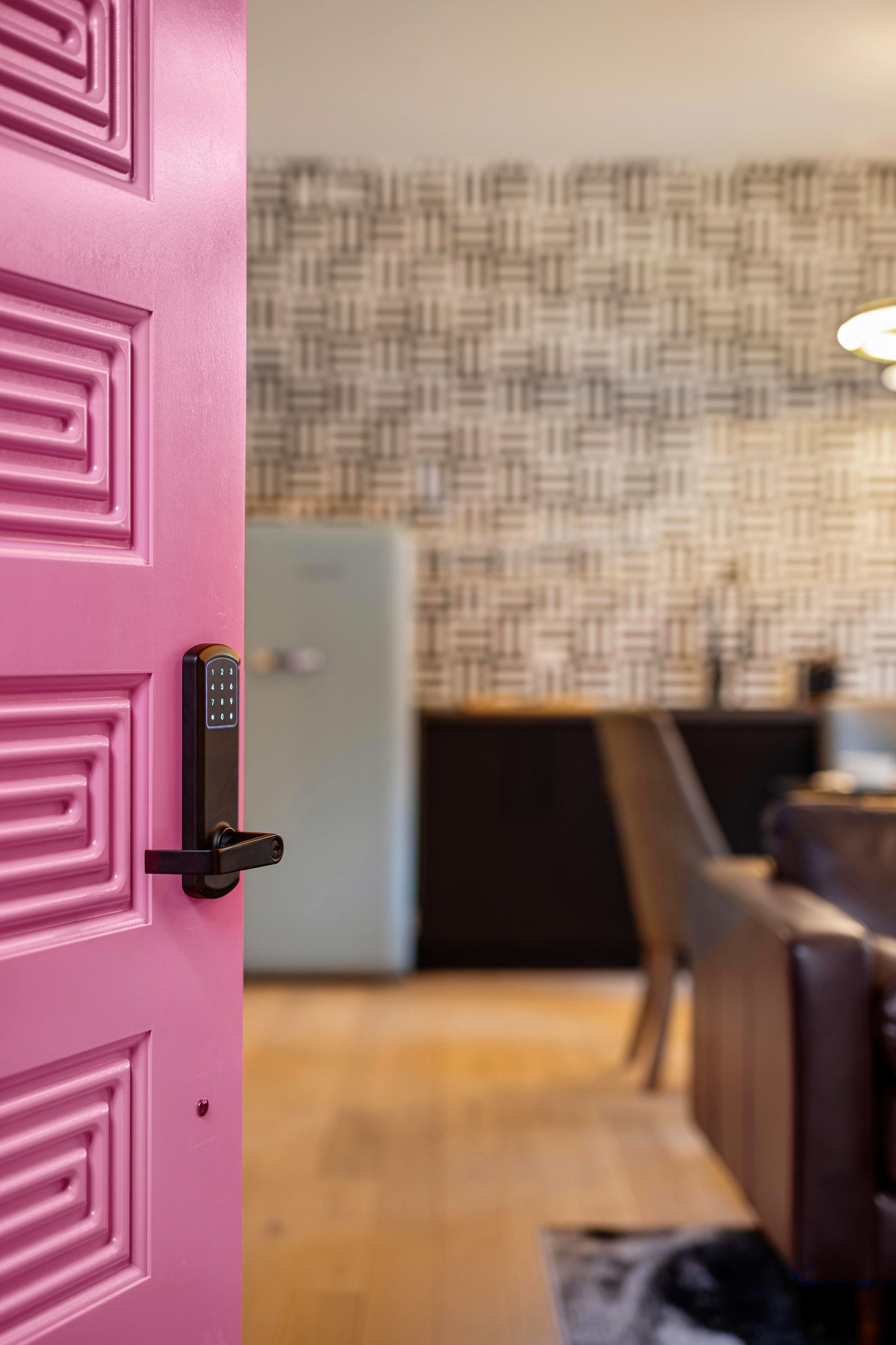 Open pink door leading to a modern dining room with patterned wallpaper and wood flooring