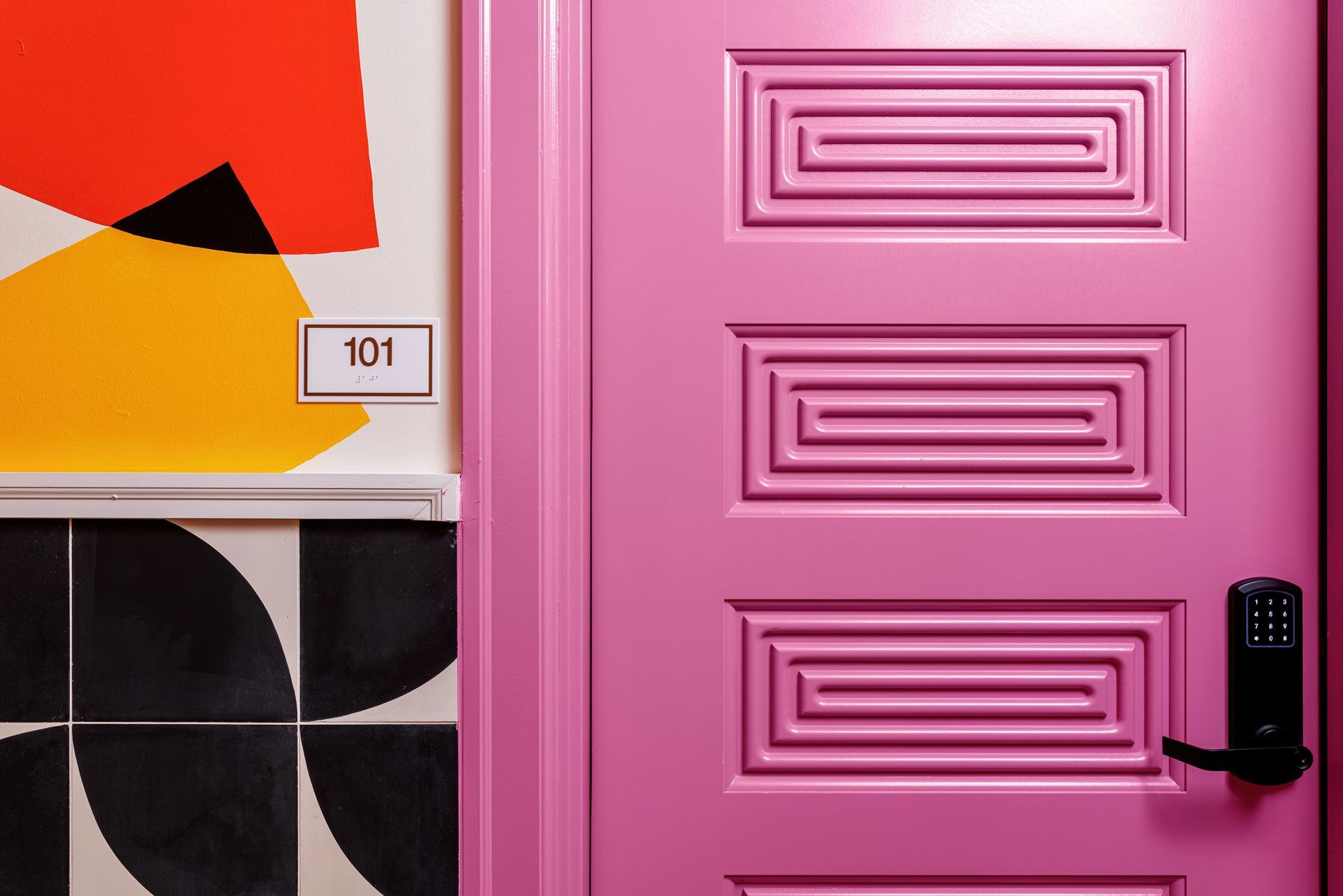 Pink door with black keypad lock beside abstract wall art and tile patterns