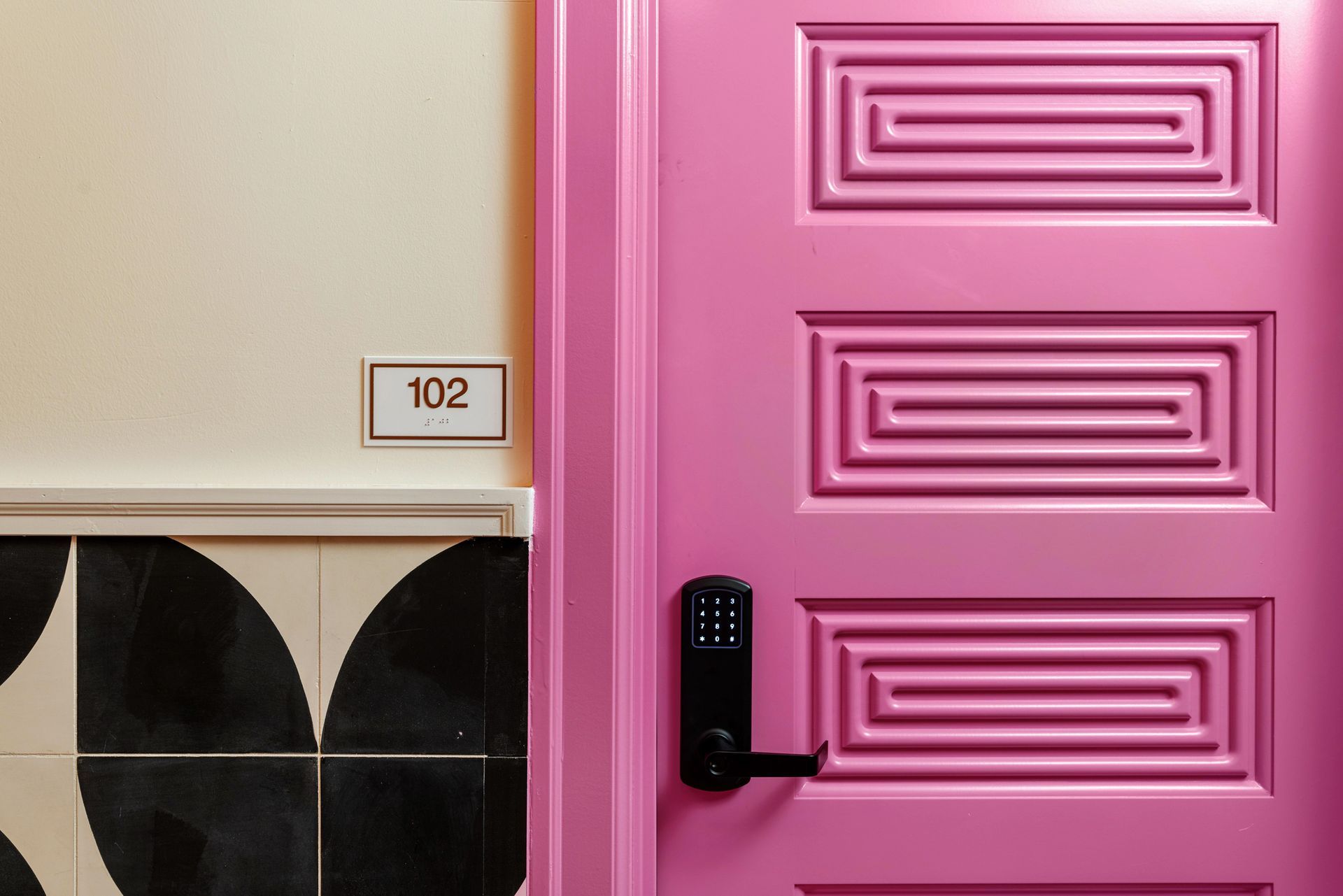 Pink front door with black handle beside a wall marked 102