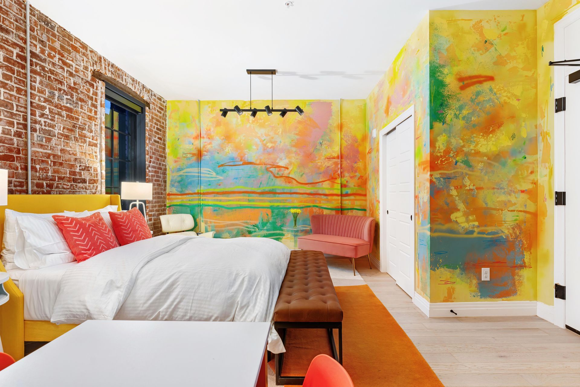 Bright colorful bedroom with exposed brick wall, white bed, and abstract painted walls and doors