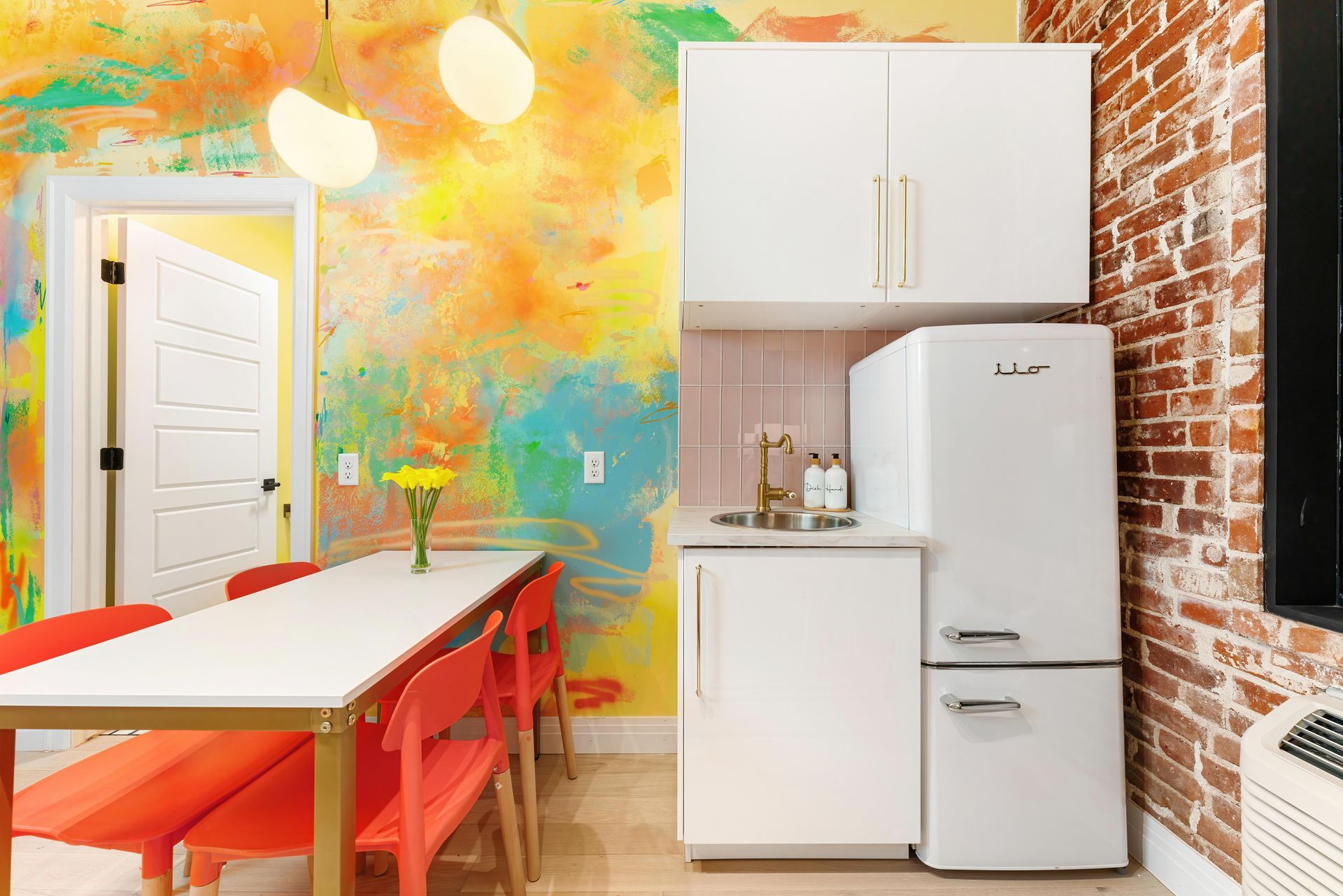 Bright kitchen-dining room with colorful mural wall, white fridge and cabinets, and red chairs around a table