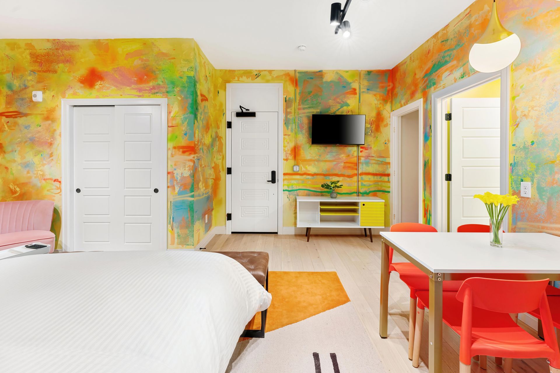 Bright colorful bedroom with white bed, orange accents, desk, wall-mounted TV, and closet doors