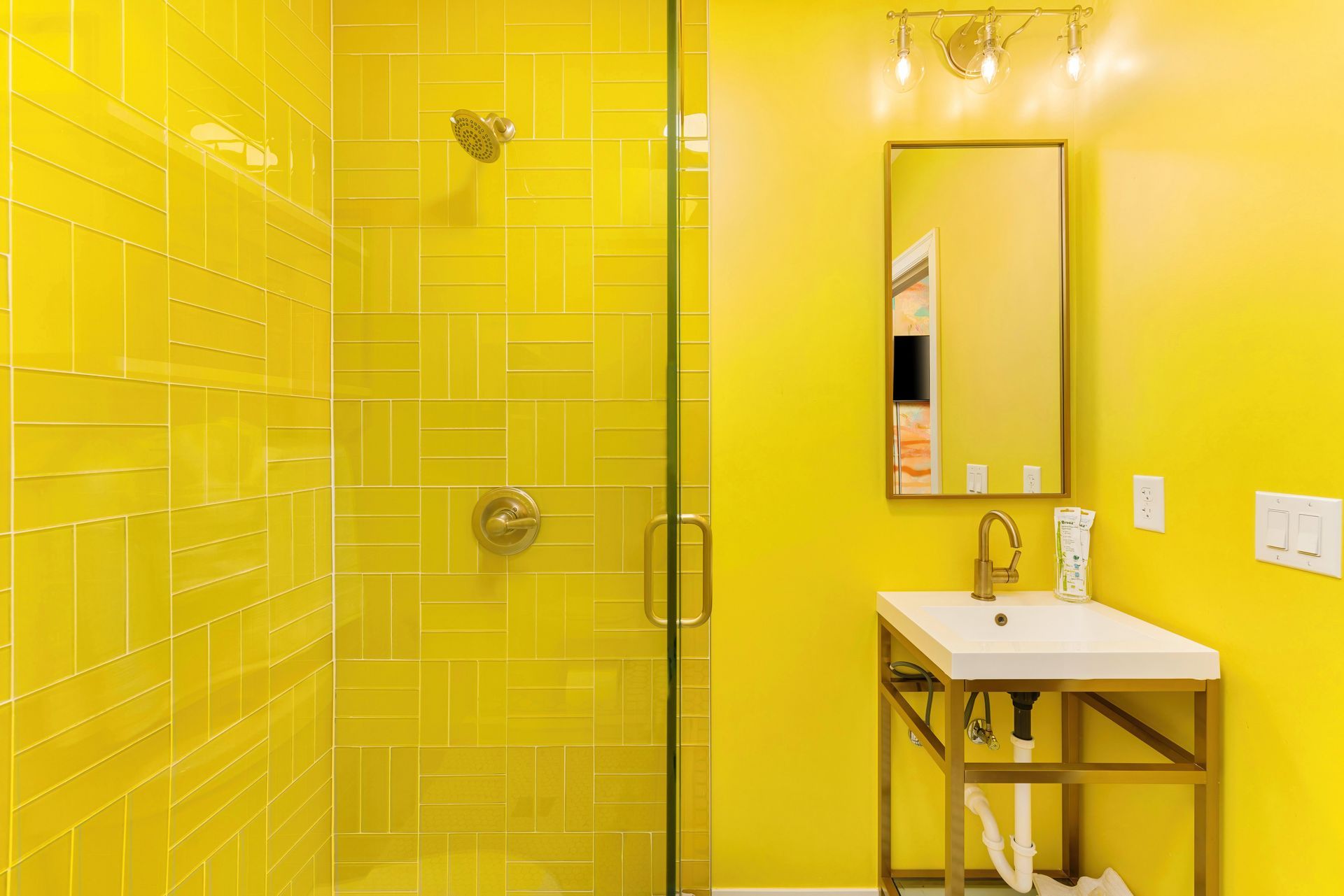 Bright yellow bathroom with glass shower, wall mirror, and small sink vanity