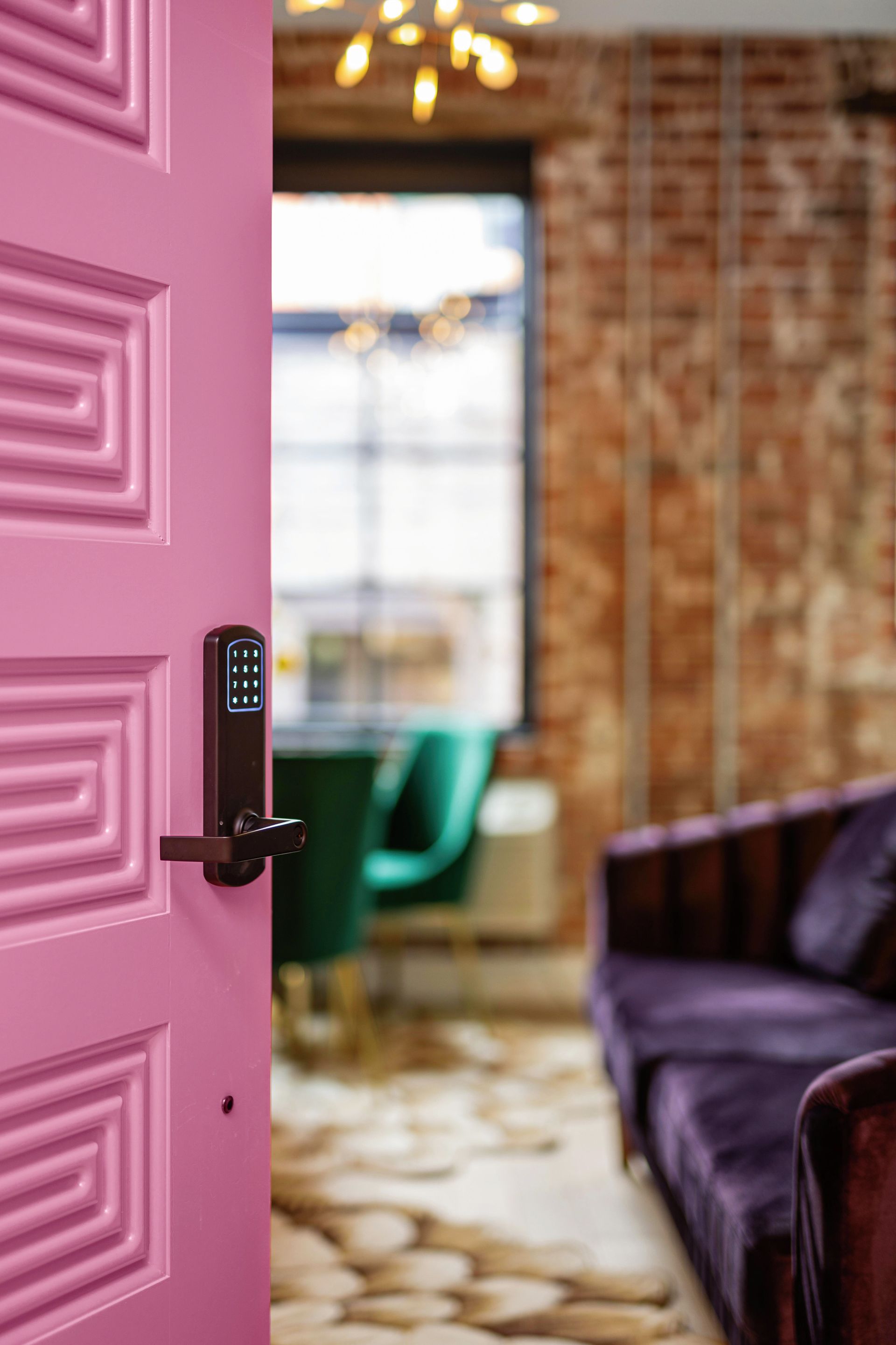 Open pink door with keypad lock leading to a cozy room with a purple sofa and brick walls