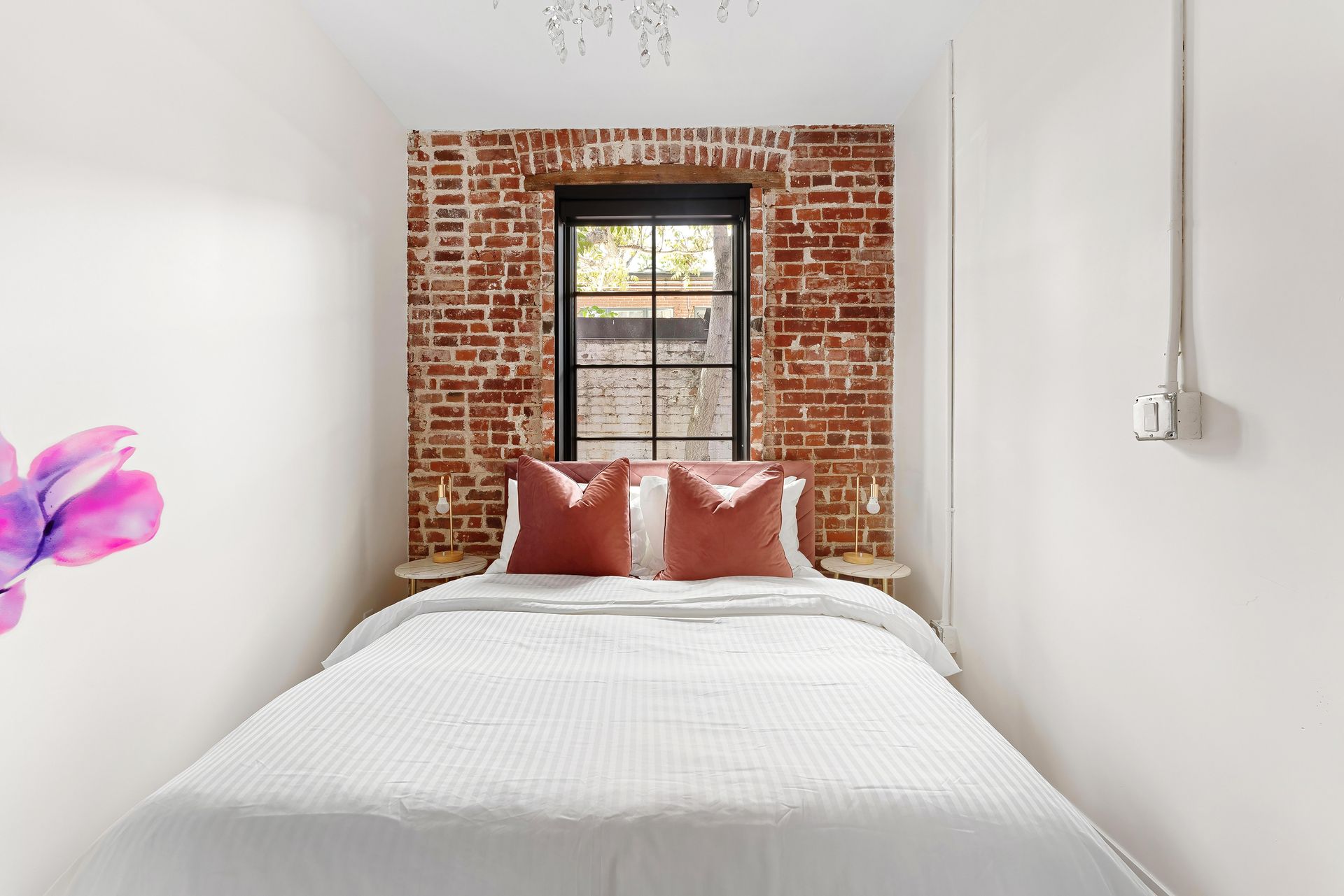 Small white bedroom with exposed brick wall, window, white bed, and pink pillows