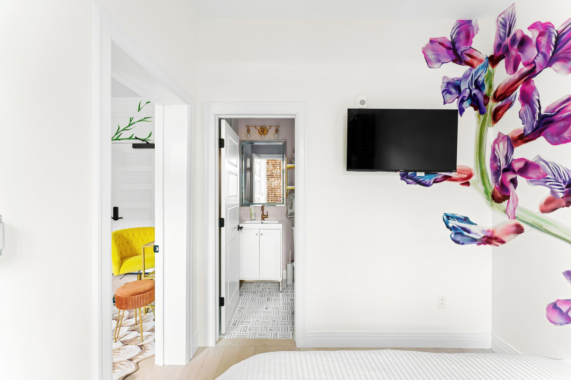 Bright white hallway with a wall-mounted TV, open doorways, and colorful floral wall art.