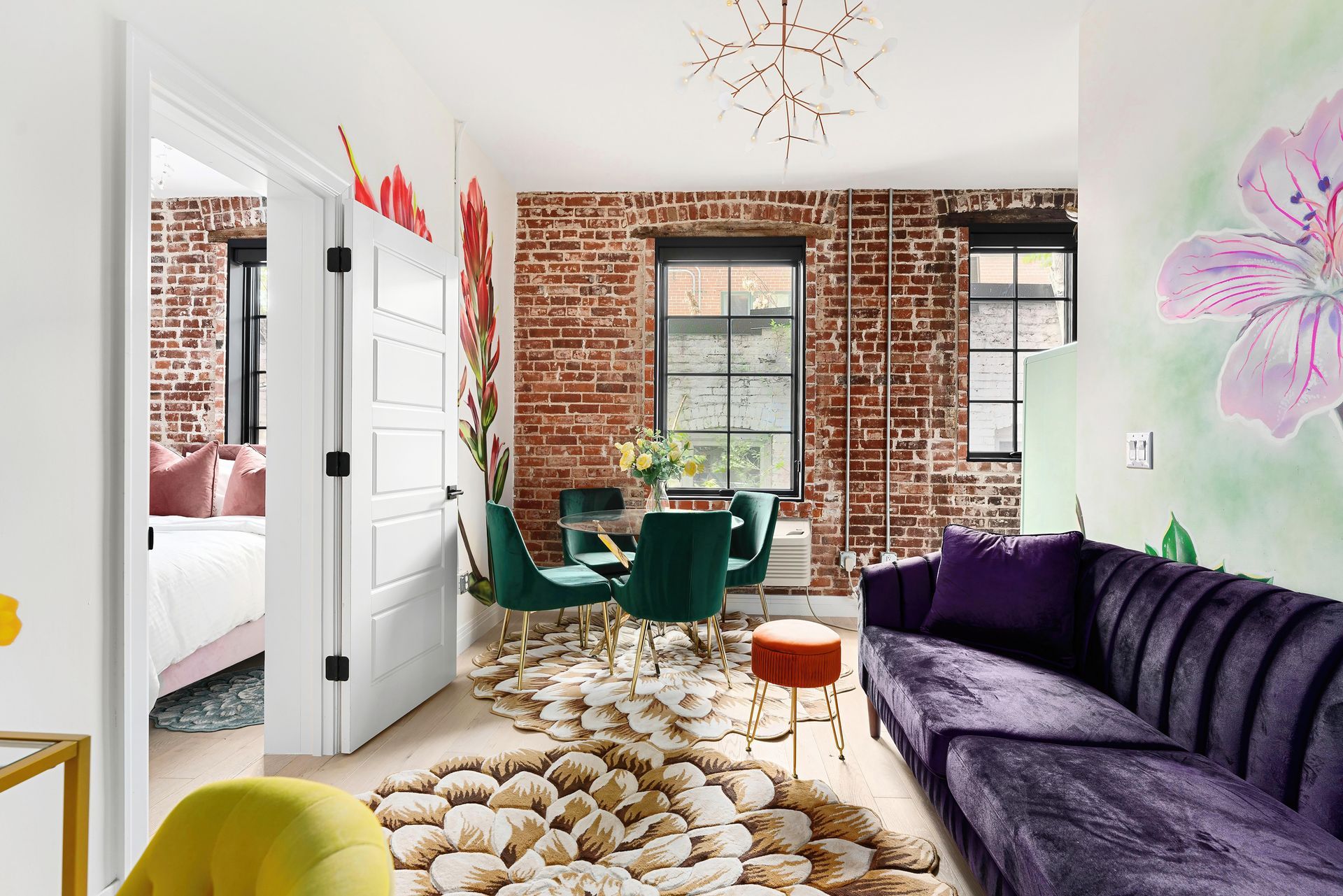 Bright living room with brick walls, purple sofa, green chairs, and a patterned rug around a window.