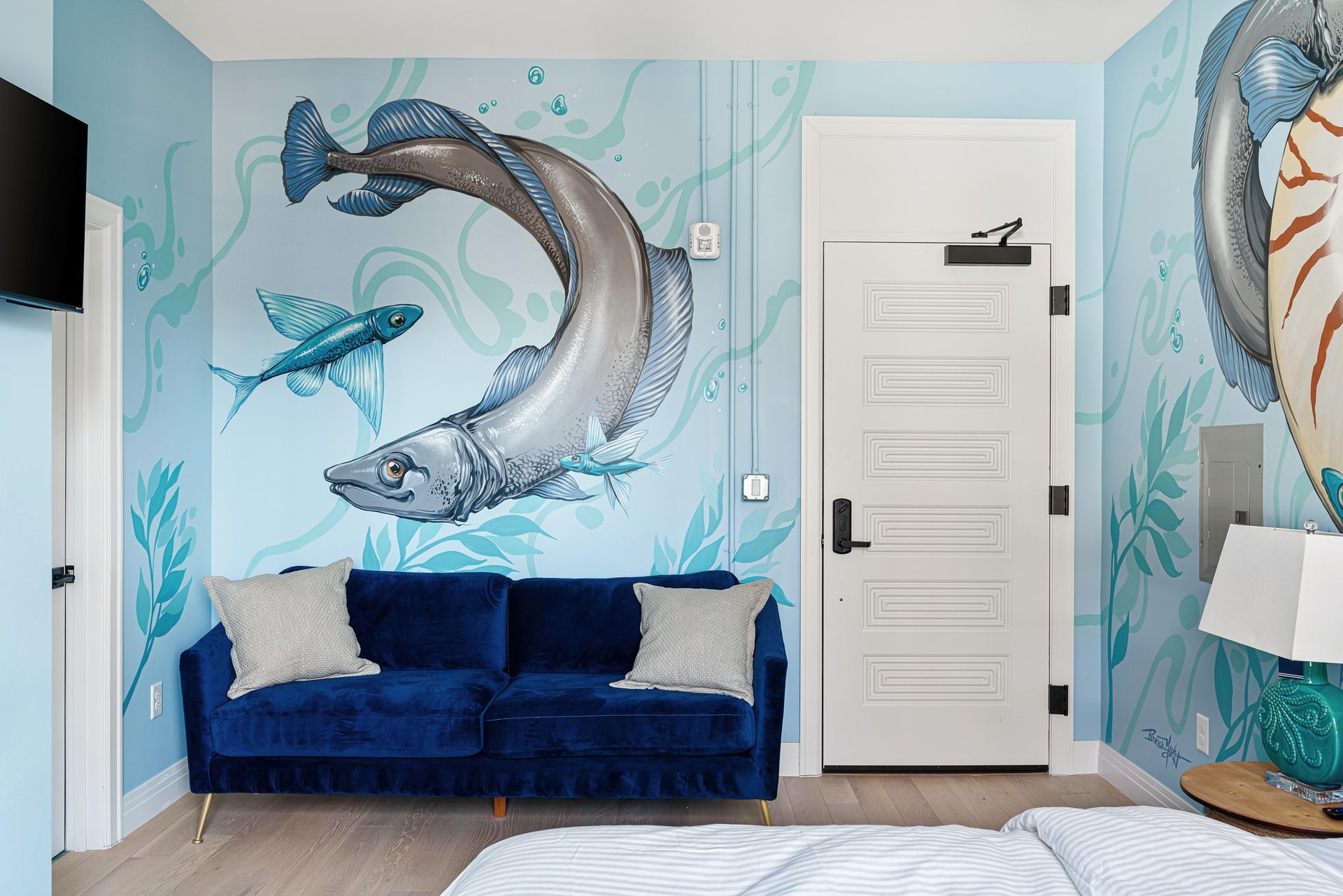 Ocean-themed bedroom with blue dolphin mural, navy sofa, and white door