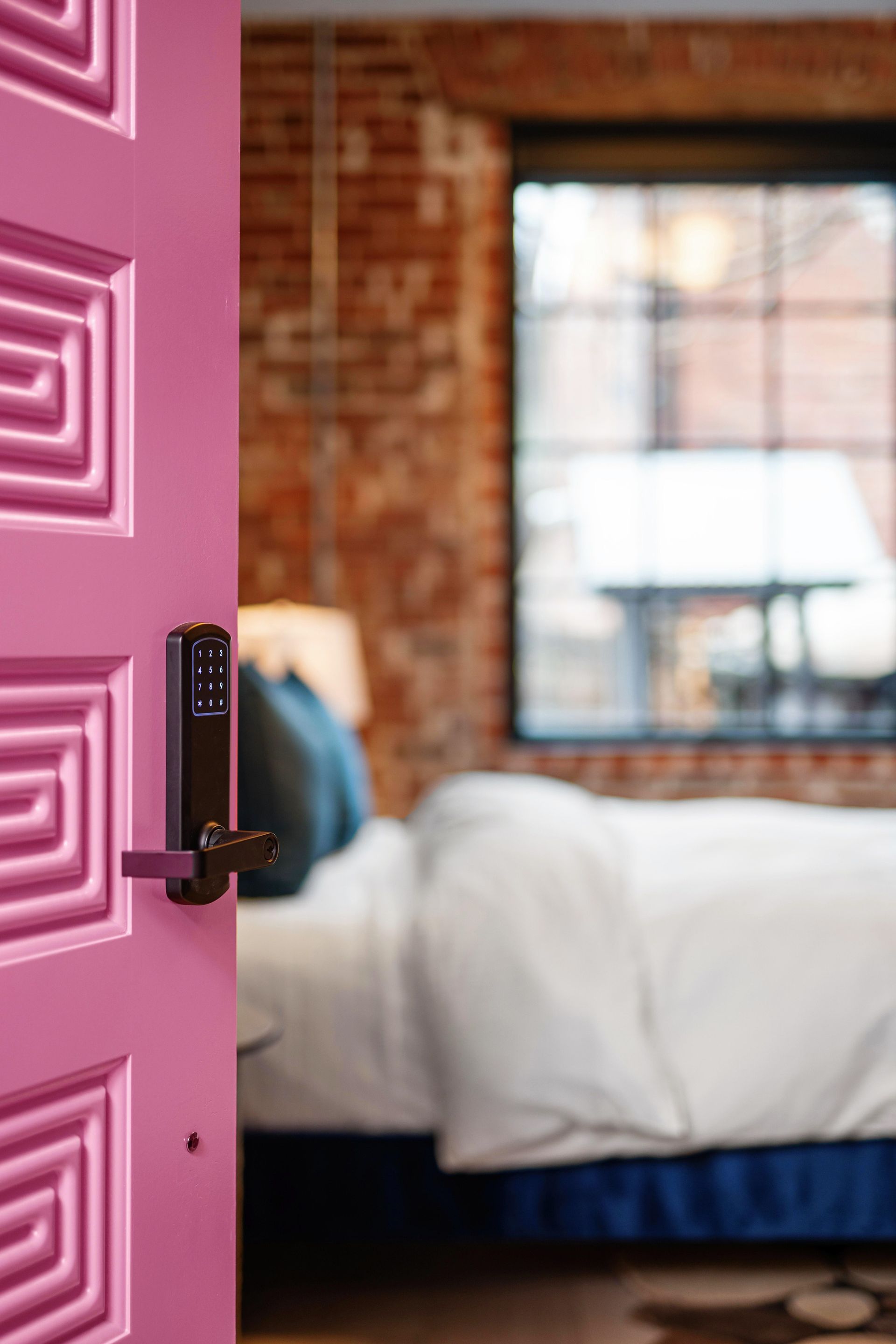 Open pink door to a cozy bedroom with a white bed and window in the background