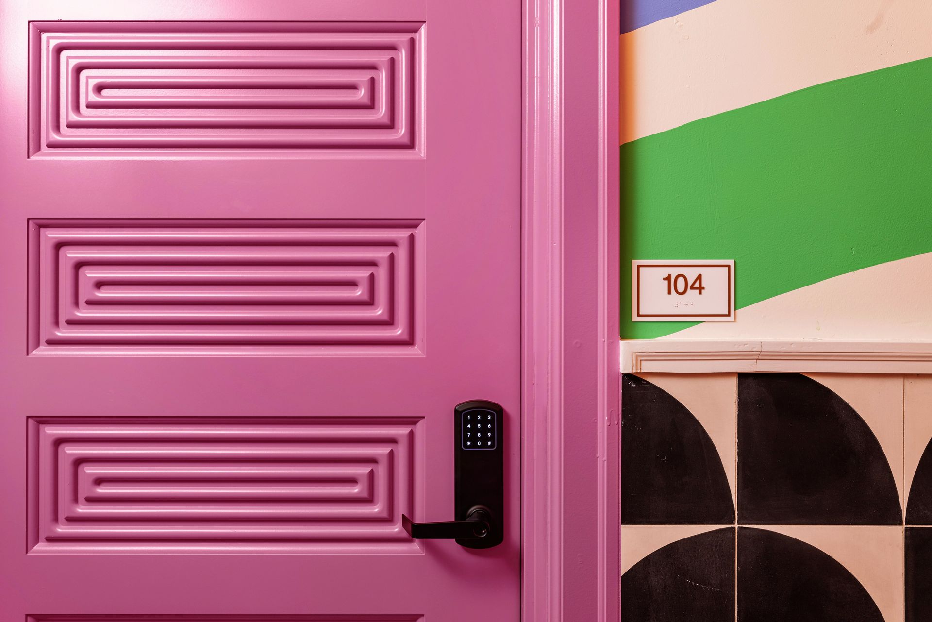 Pink paneled door with black handle beside a green-and-beige wall and a small room number sign 104