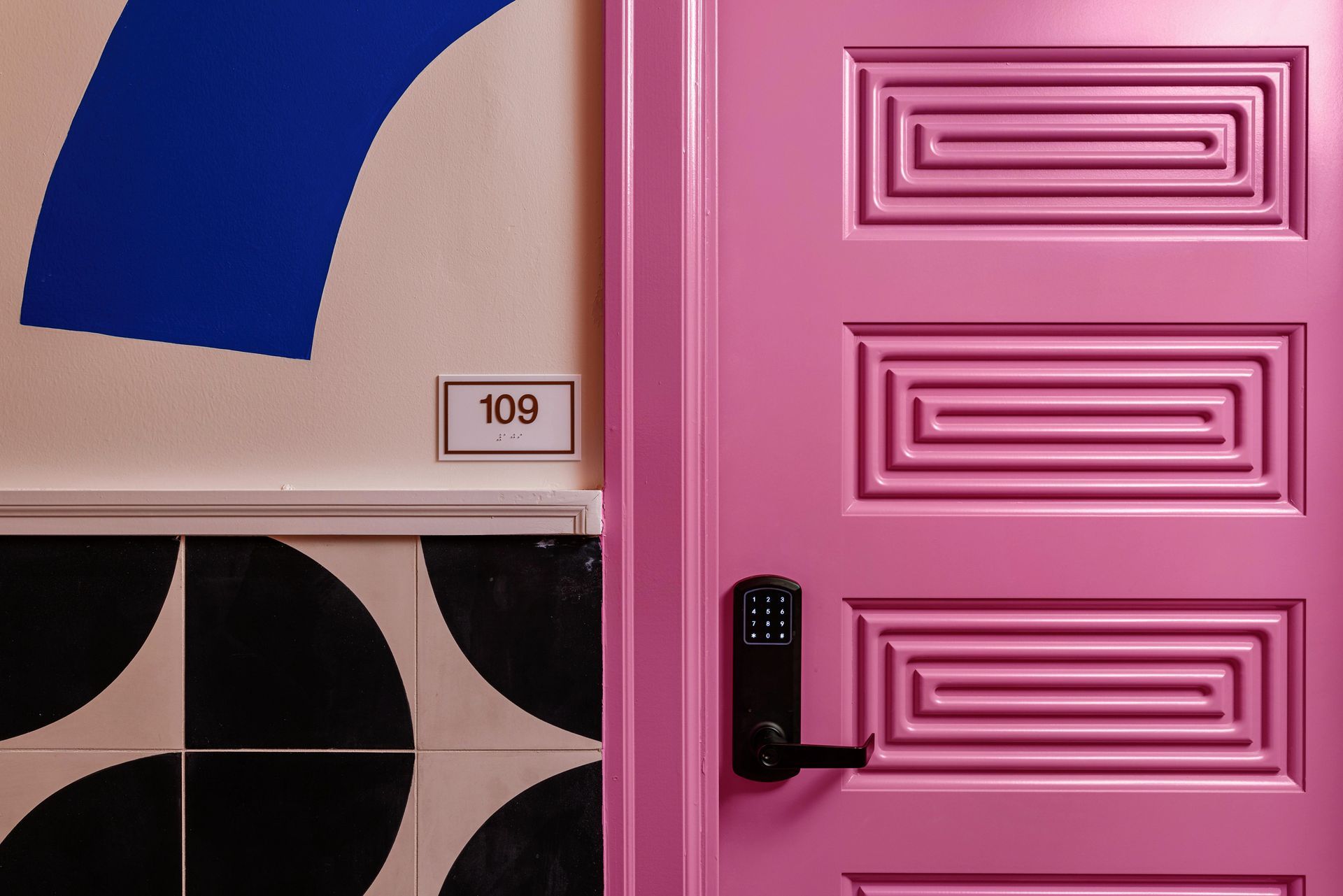Pink door with black handle beside geometric wall and room number 109
