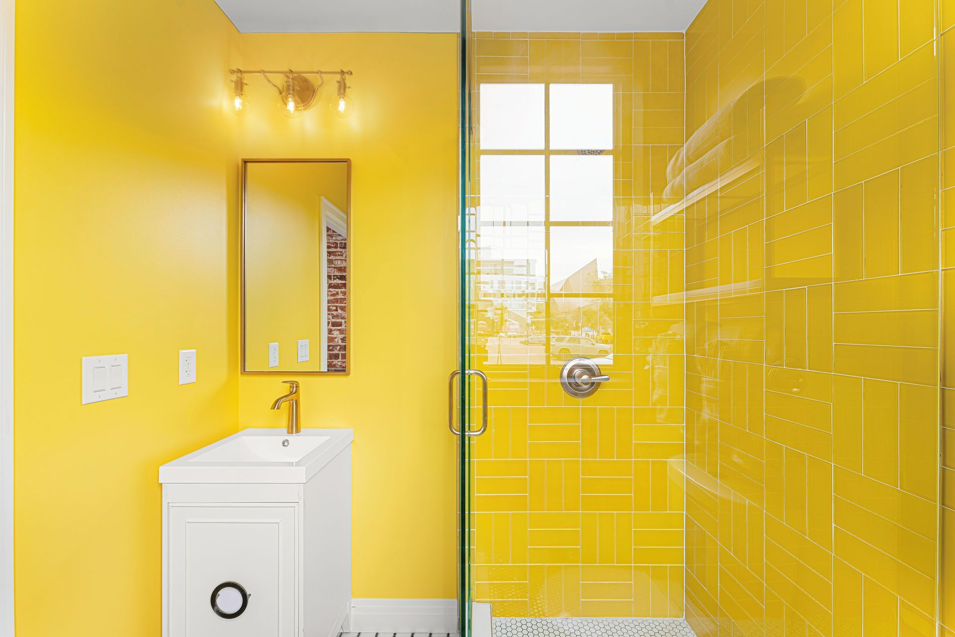 Bright yellow bathroom with a sink, mirror, and glass shower door.