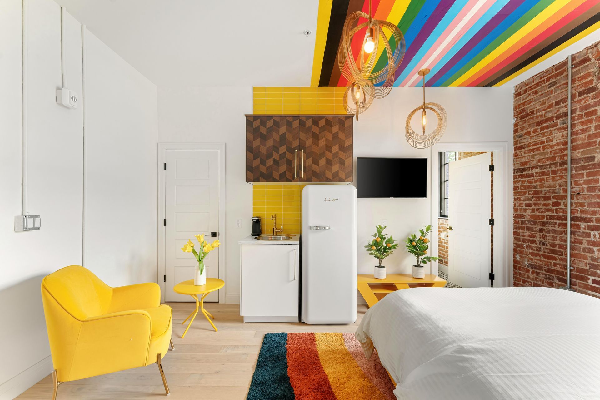 Bright modern bedroom with yellow chair, white walls, rainbow ceiling, and colorful rug